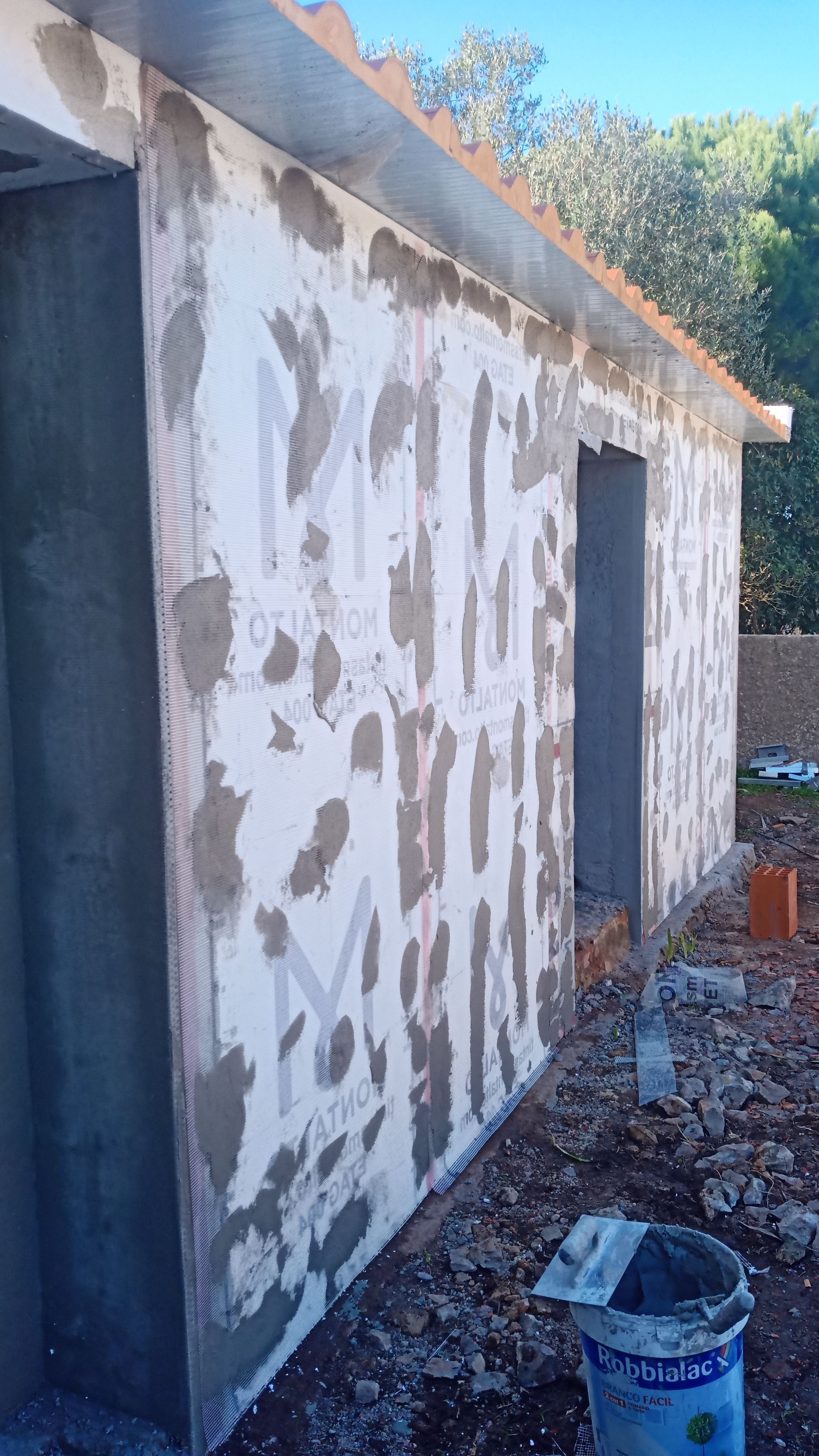 Parede externa em construção, com argamassa e tela aplicadas na superfície.
