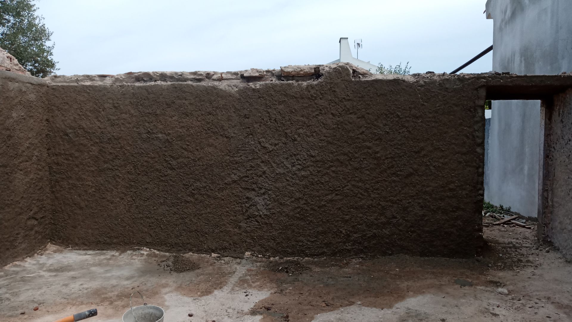 Parede externa de um edifício com reboco escuro e áspero. Uma porta aberta é visível à direita.
