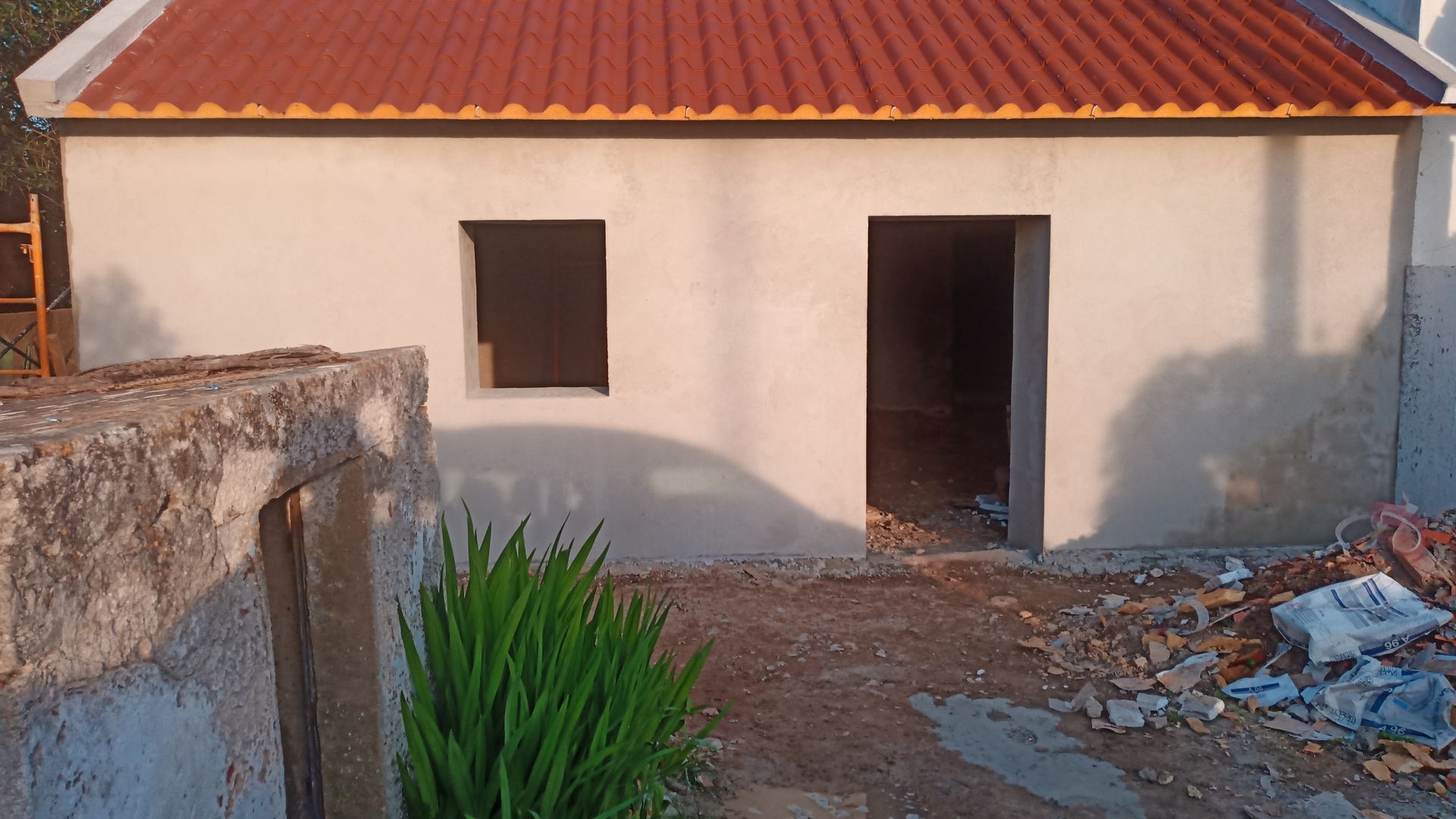 Pequeno prédio em construção, sem pintura, com telhado, janelas e portas na cor vermelha.