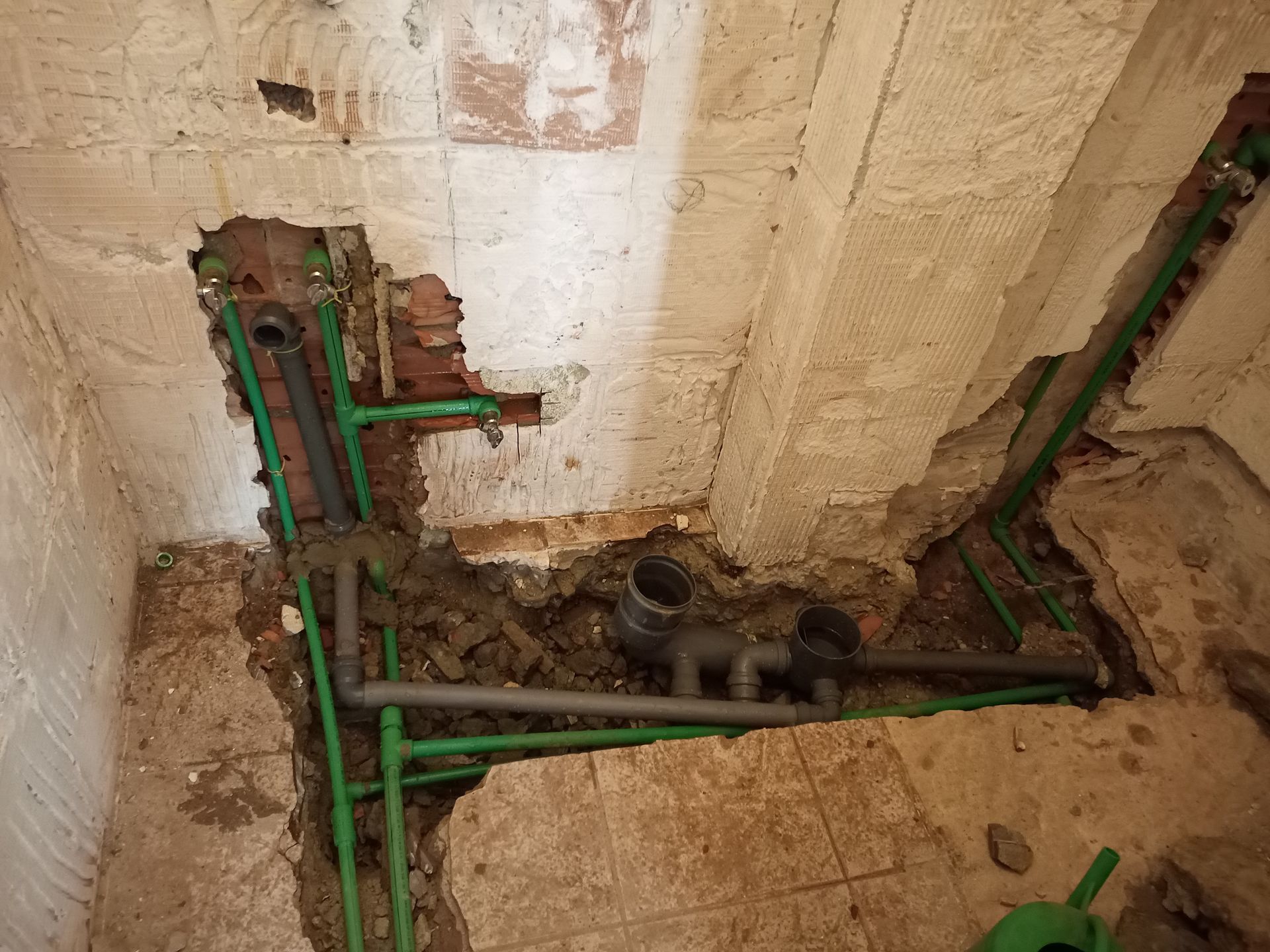 Tubulações de encanamento verdes e cinzas expostas em uma parede durante a construção.