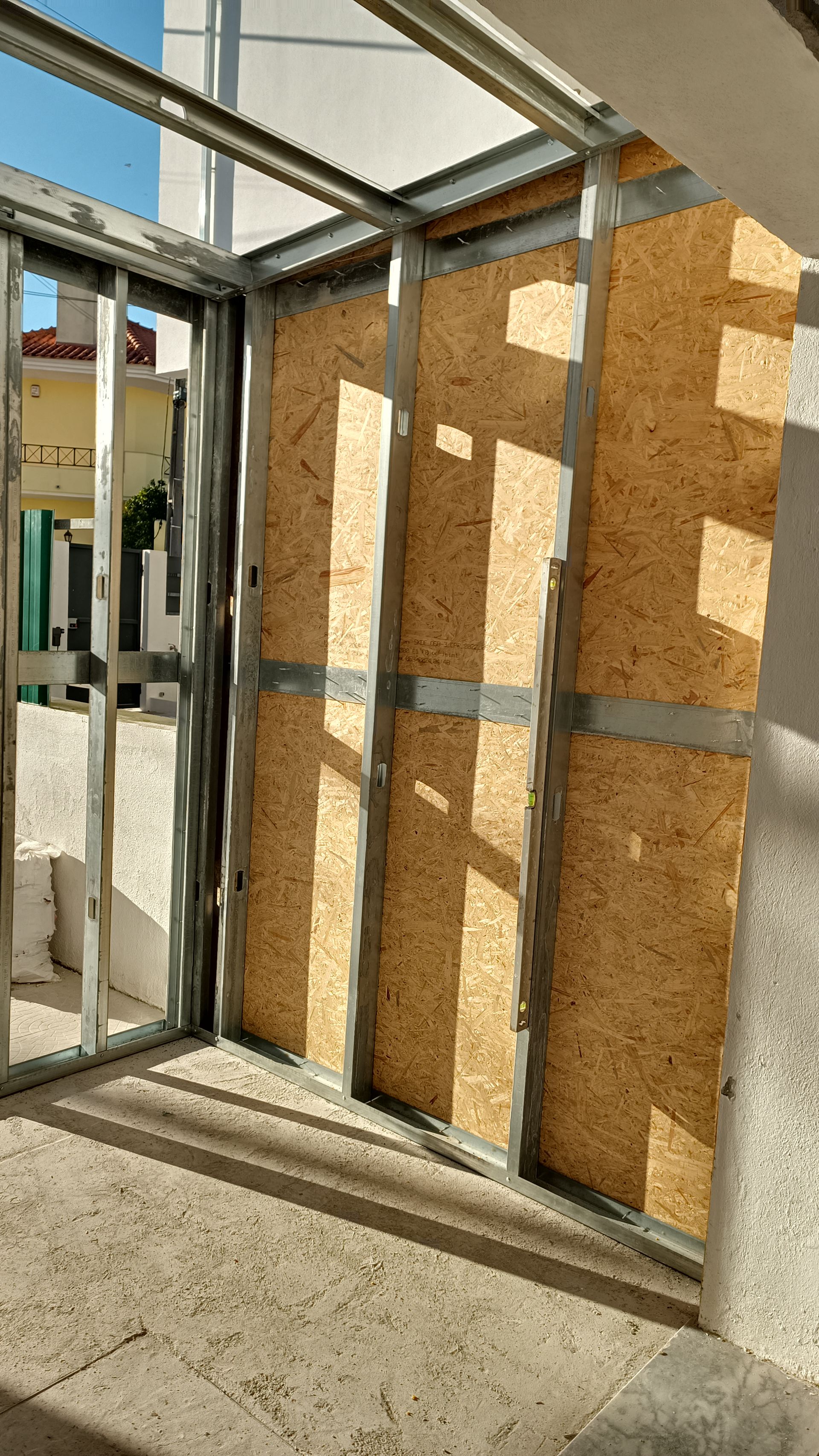 Estrutura metálica com painéis de madeira orientada (OSB) para uma porta. Luz solar intensa, ambiente externo.