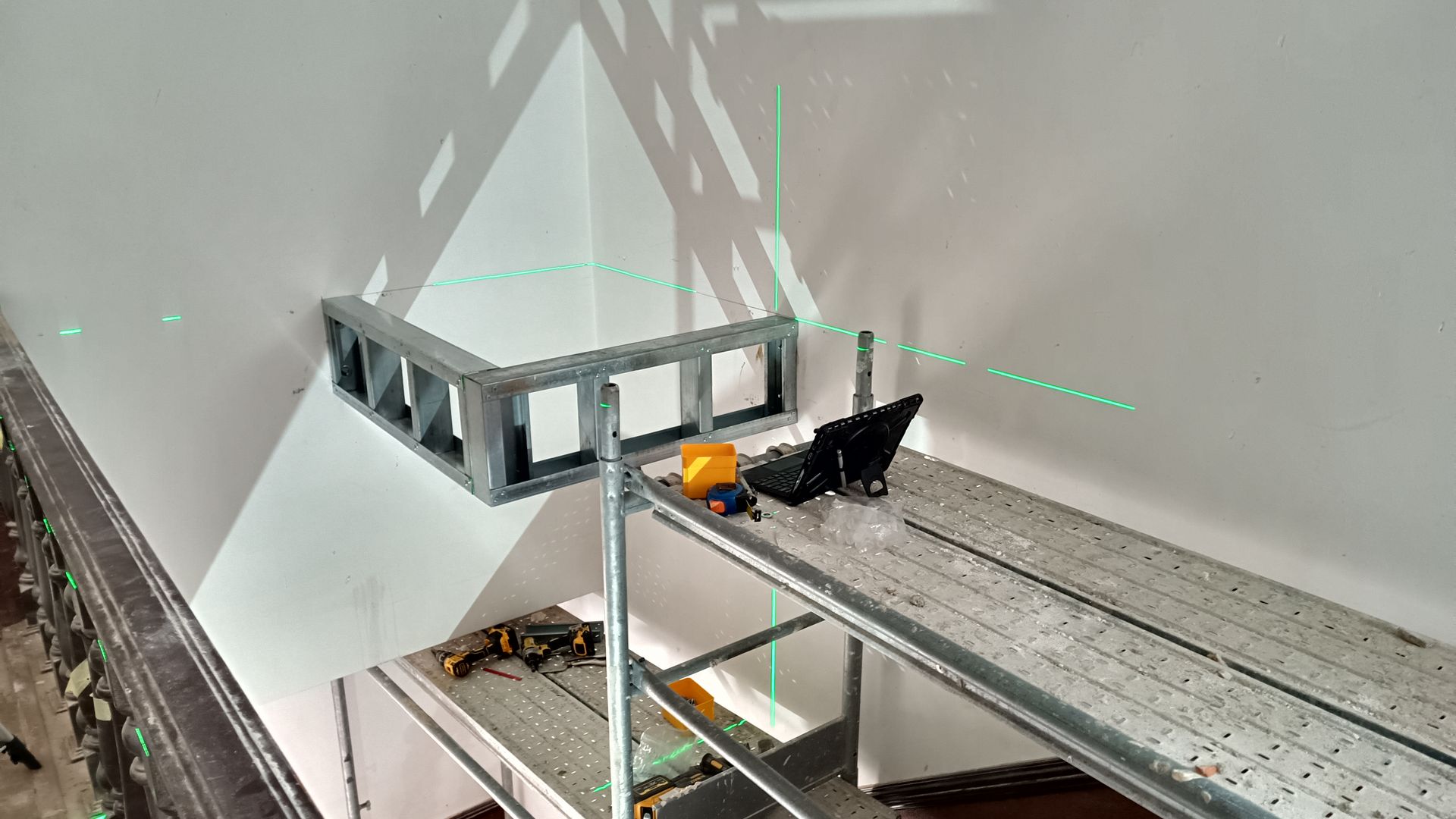 O nível a laser projeta linhas verdes nas paredes, na estrutura metálica no canto e no andaime.