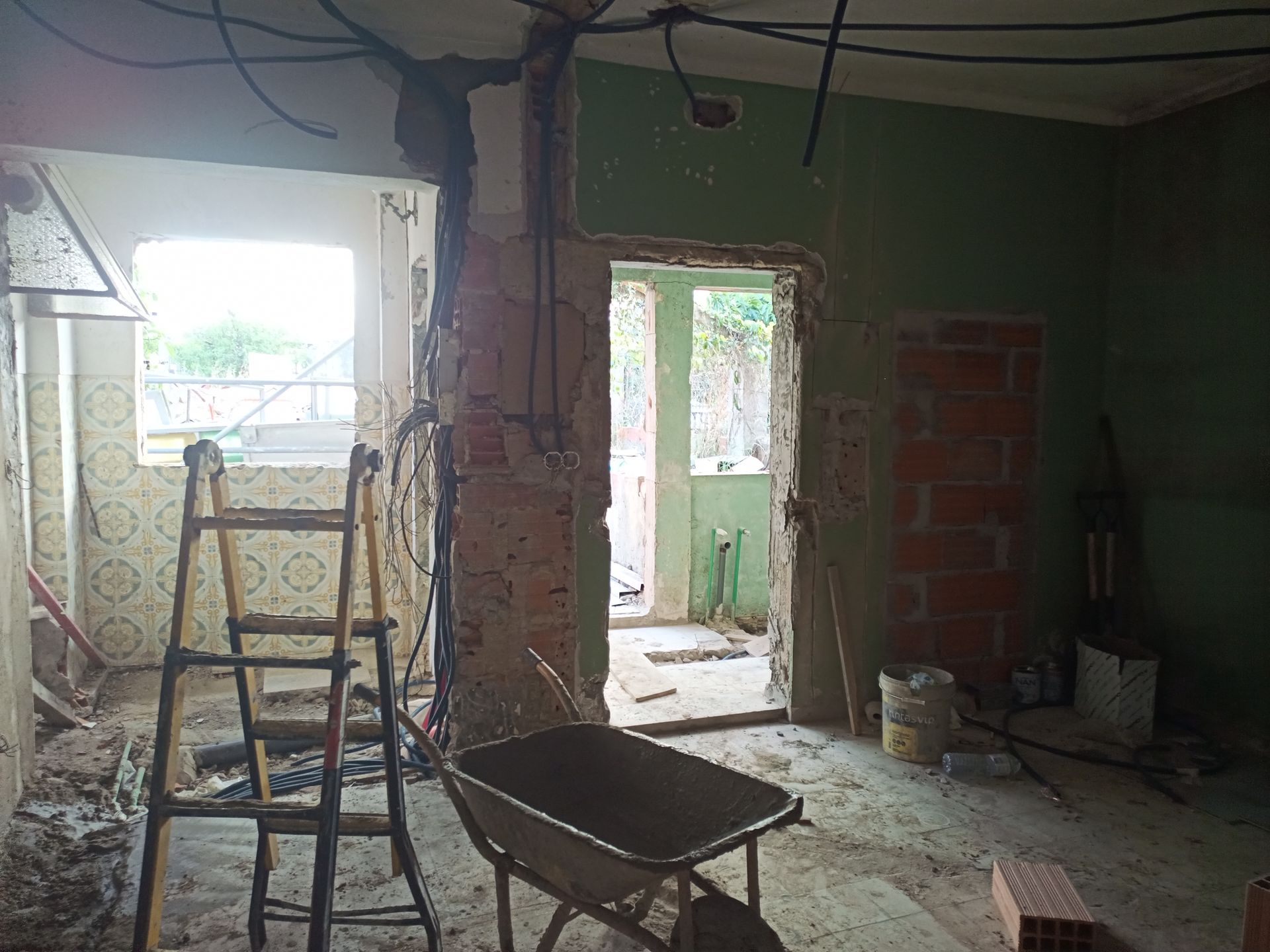 Quarto interior em reforma, com fiação exposta, escada e carrinho de mão.