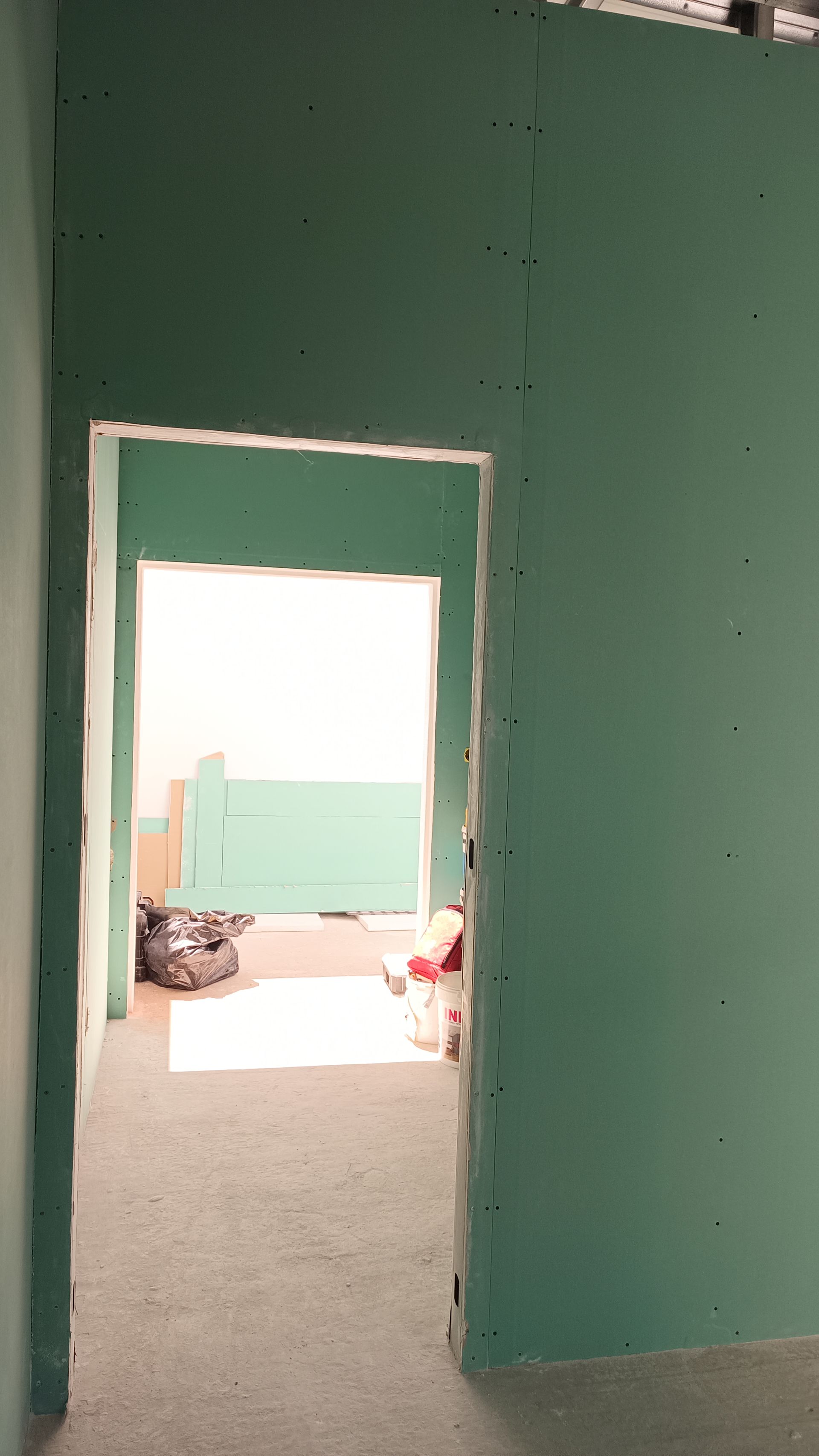 Interior de um cômodo em construção, com uma porta que dá acesso a outro cômodo; parede de gesso verde; piso cinza.