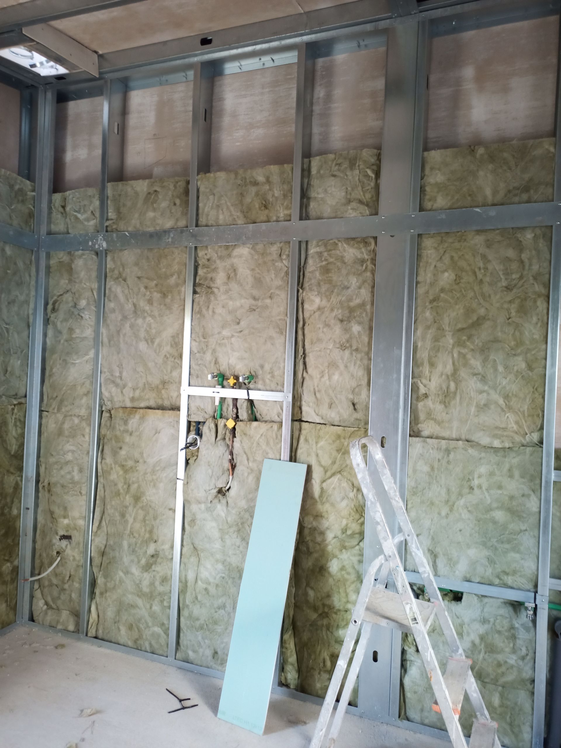 Parede interna em construção com estrutura metálica, isolamento e escada.