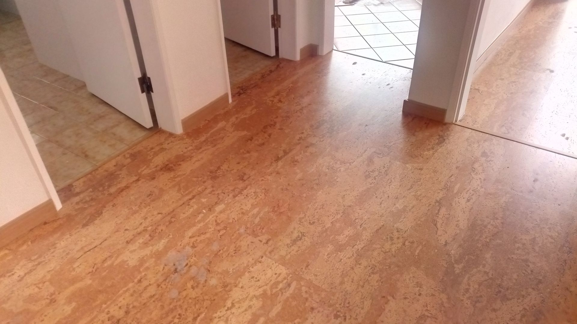 Piso de cortiça em um corredor. Portas e área com azulejos visíveis.