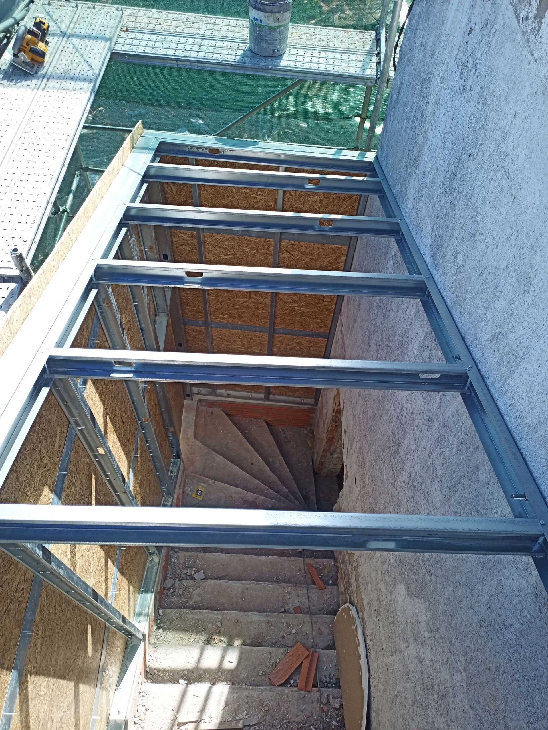 Vista aérea de uma estrutura metálica sobre uma escadaria de pedra, que desce em direção a uma escada em espiral.