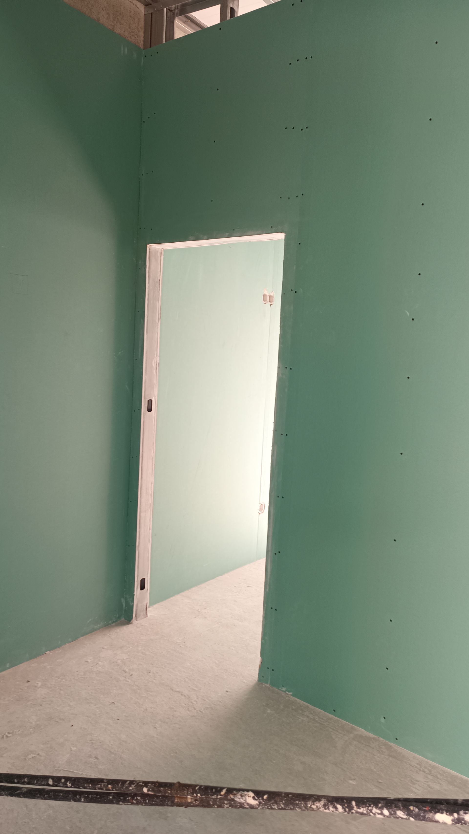 Parede de gesso verde em um cômodo com porta.