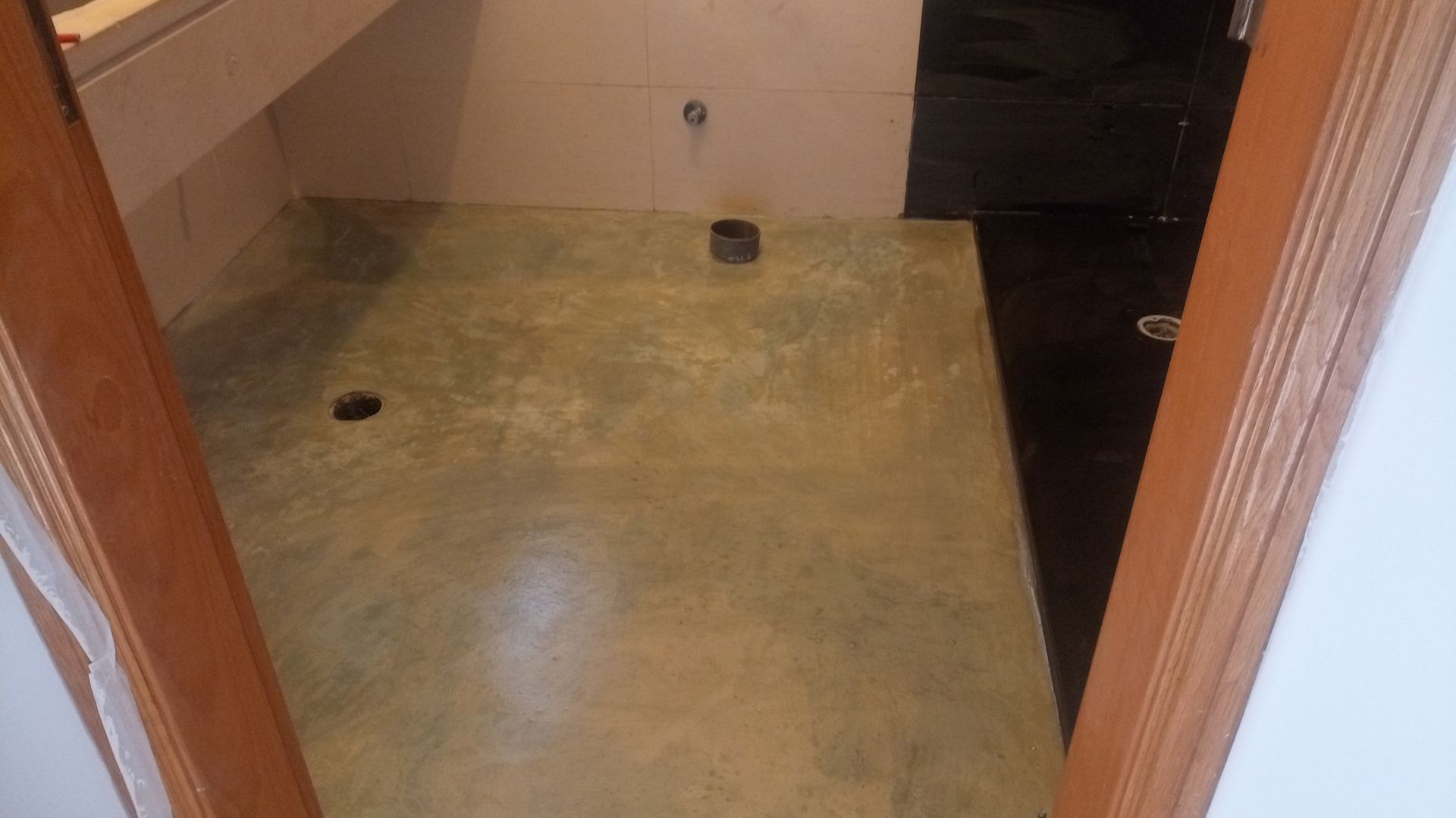 Banheiro com piso de concreto pigmentado, área escura, dois ralos e porta.