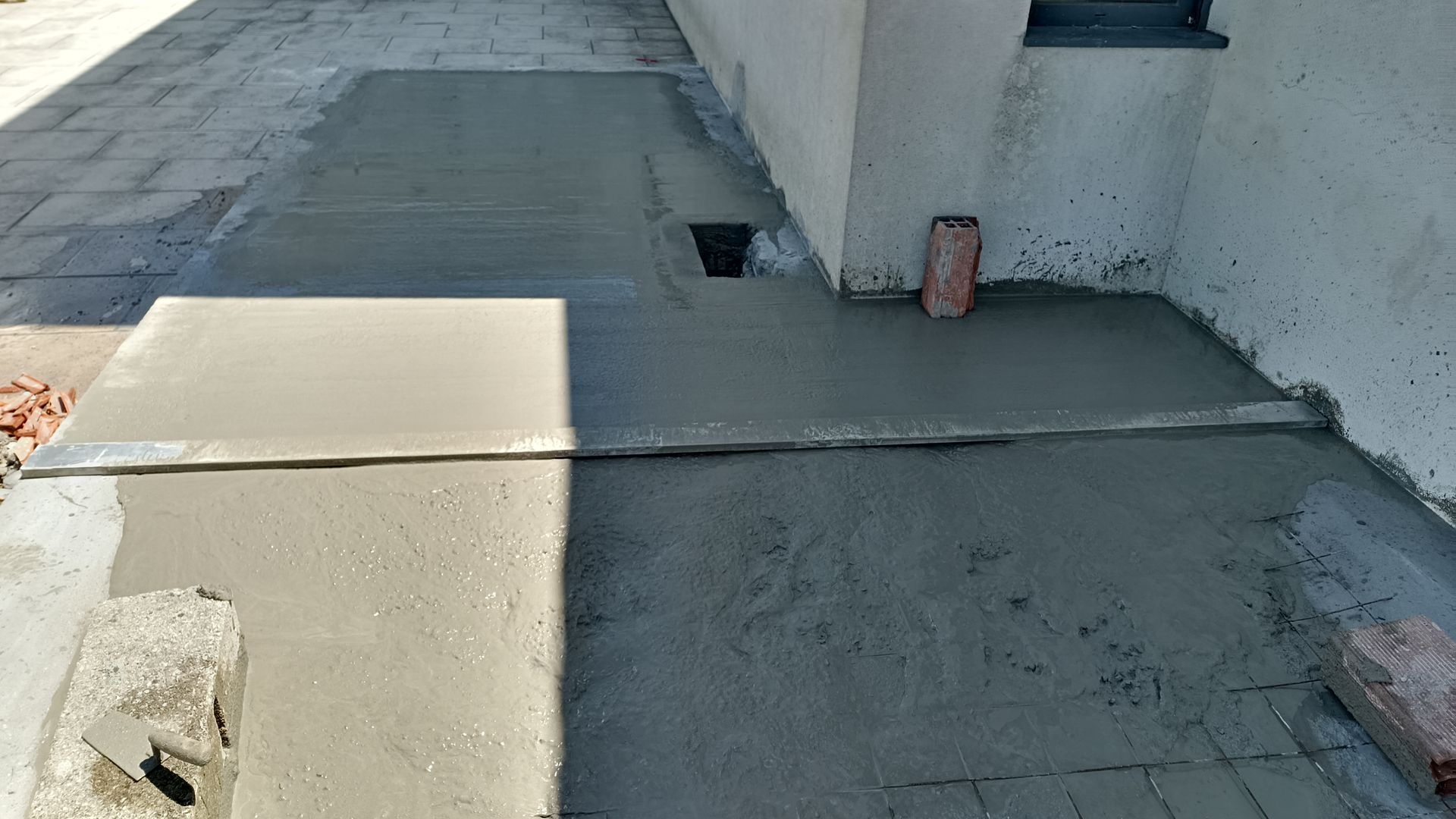Concreto recém-lançado em uma superfície inclinada ao lado de um edifício; inclui um ralo.