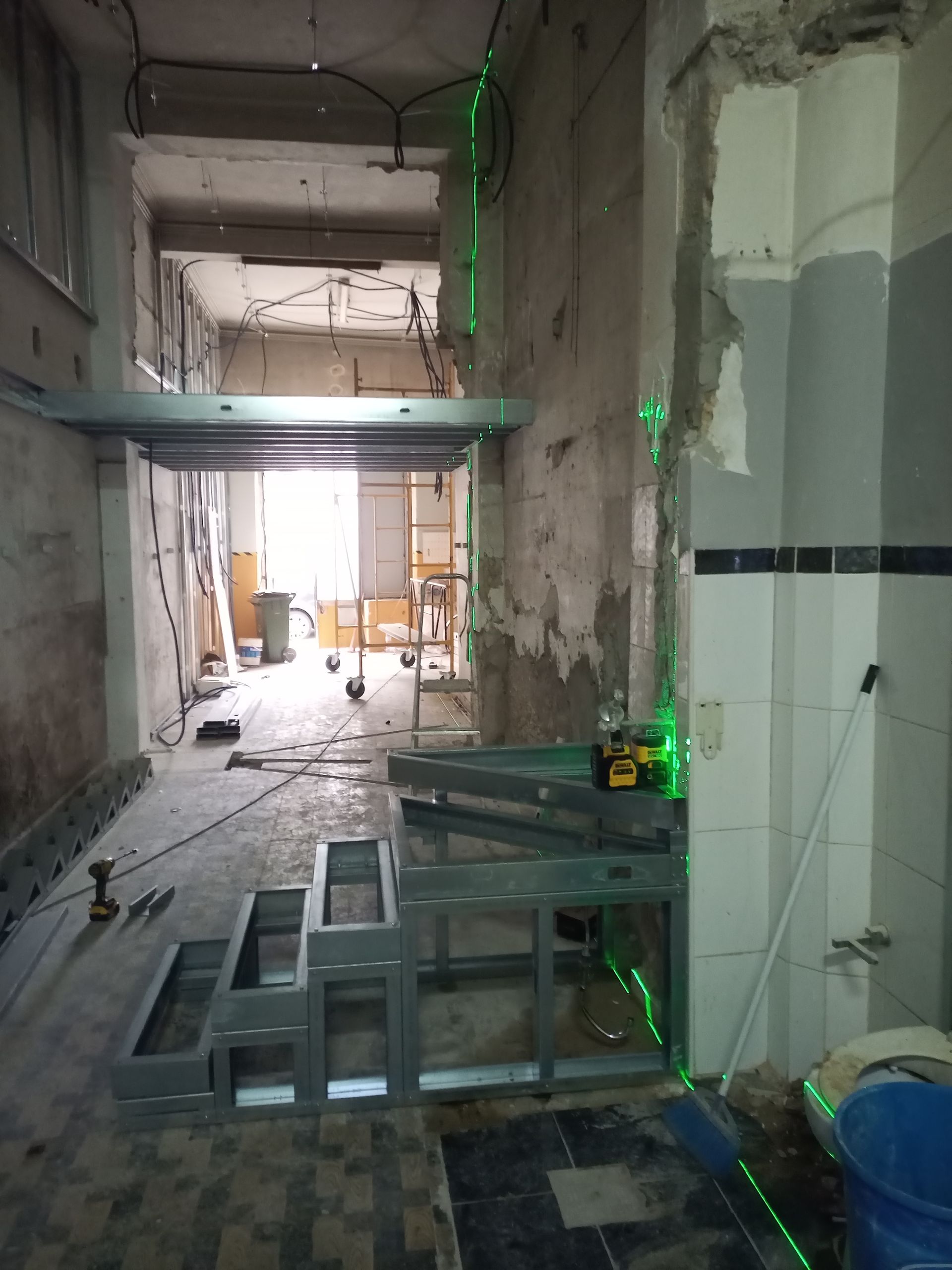 Canteiro de obras: degraus e prateleiras com estrutura metálica, linhas de nível a laser, paredes inacabadas e entulho.