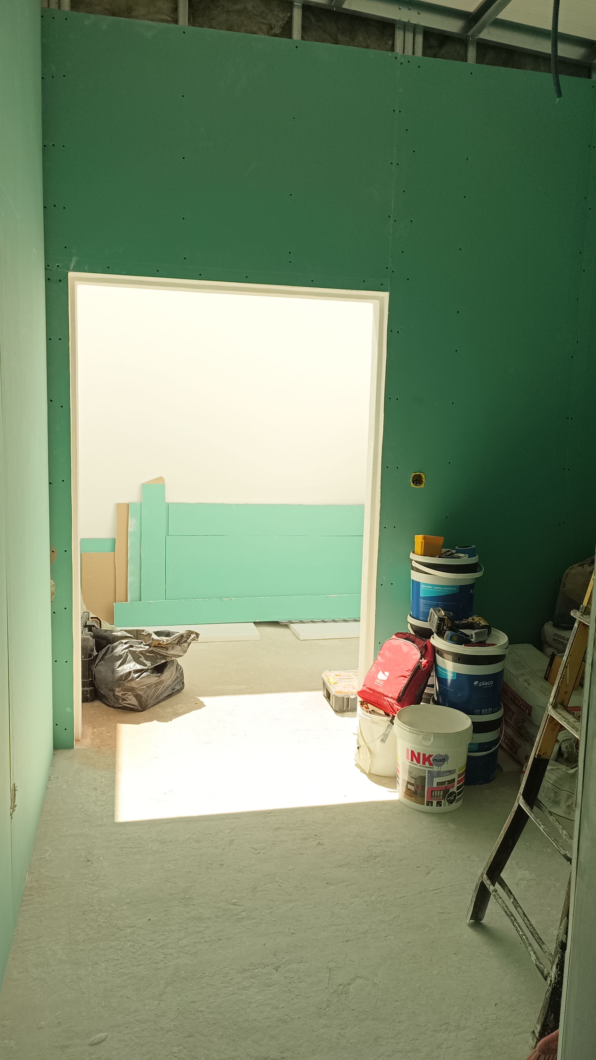 Construção de interiores com paredes verdes e uma porta, latas de tinta e uma escada.