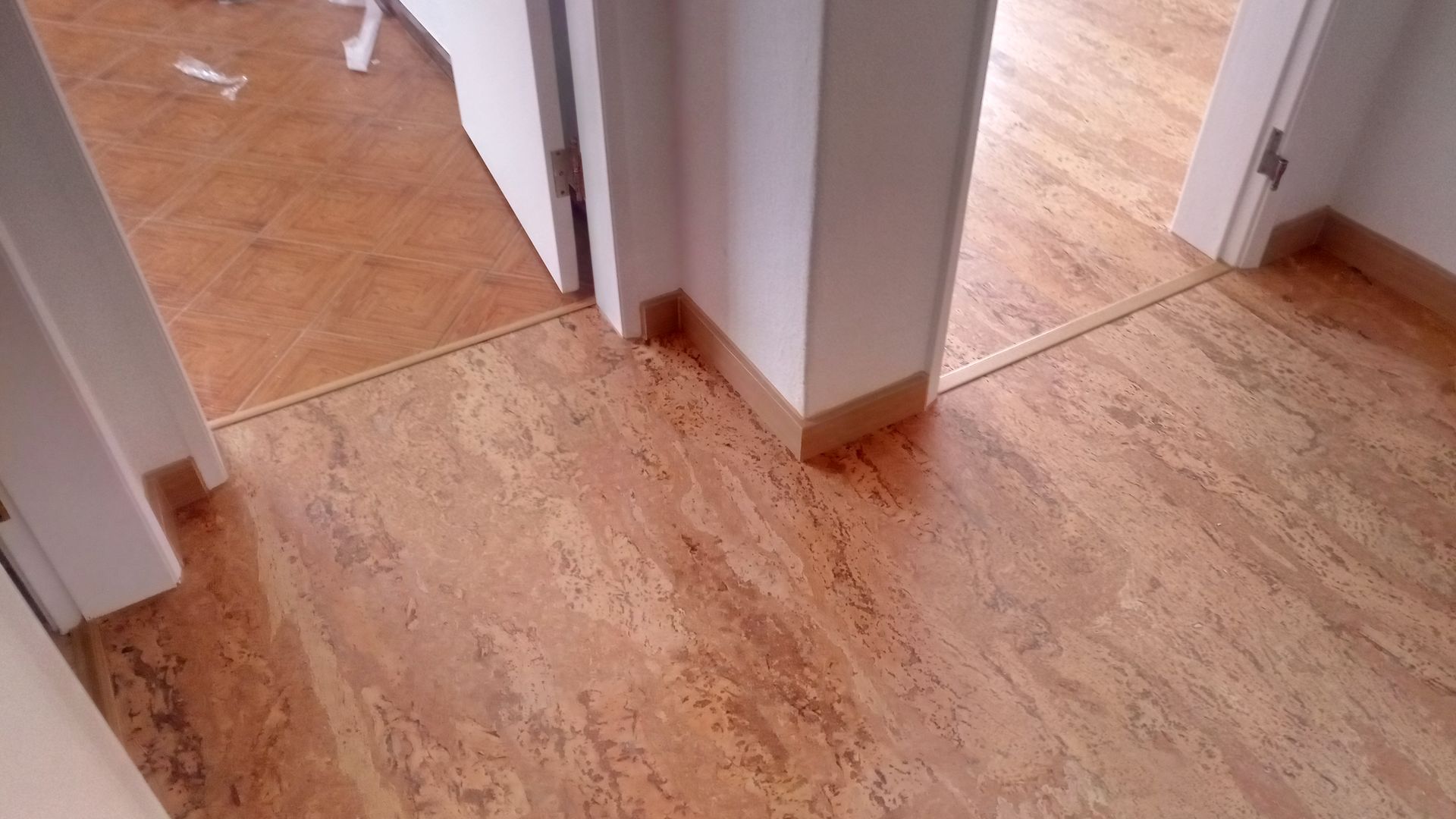 Piso de cortiça em uma porta. Piso e rodapés em tom bege encontram uma coluna e porta brancas.