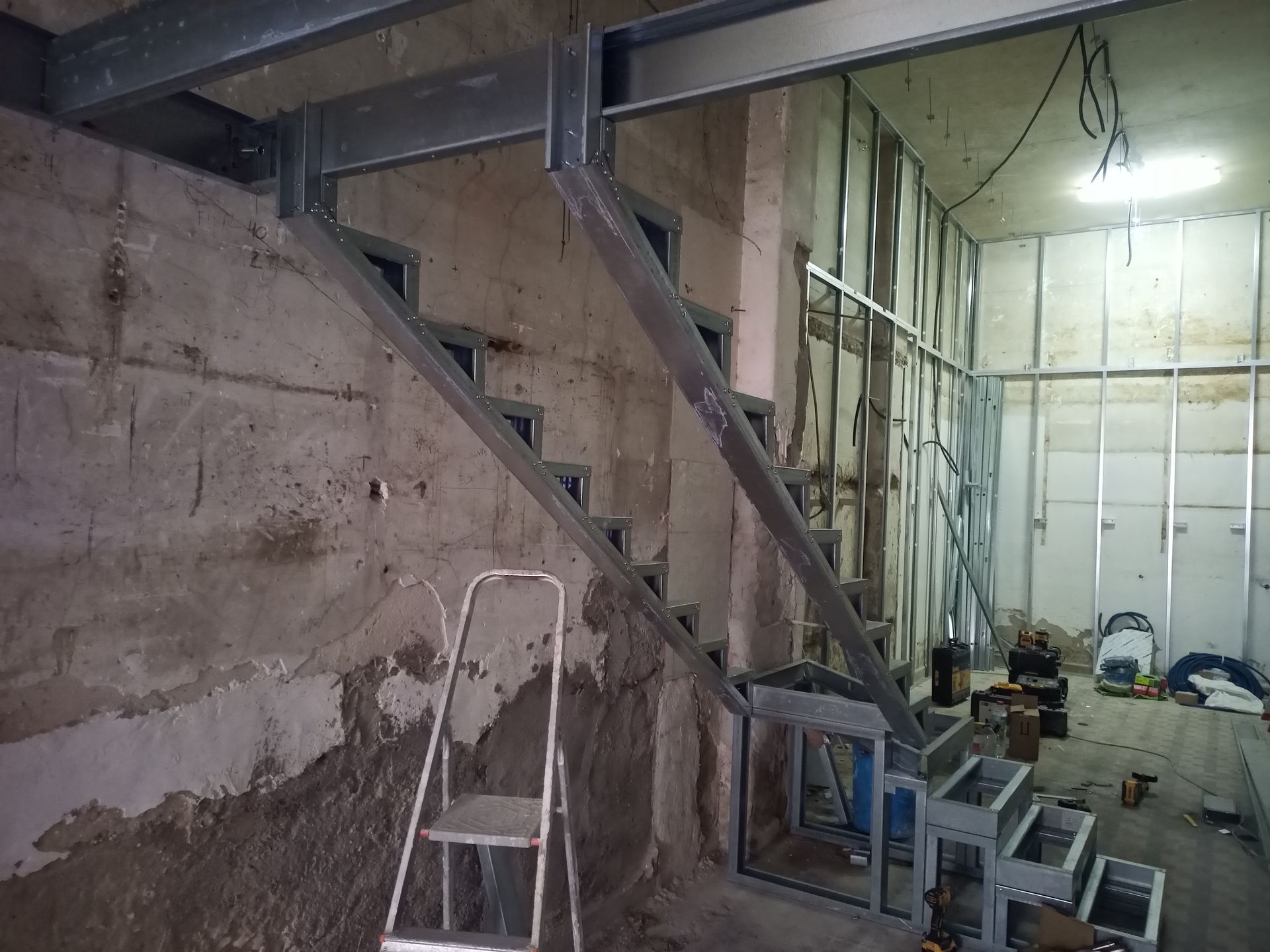 Escada de aço em construção em uma sala com paredes e teto inacabados.