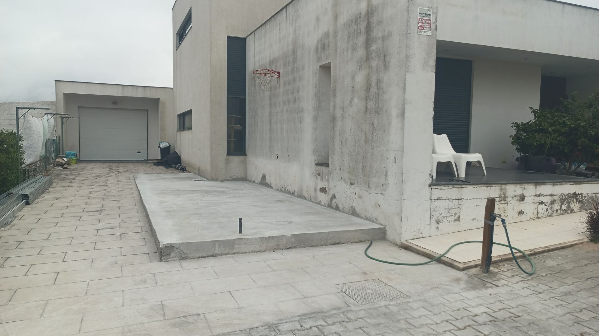 Casa moderna com entrada de automóveis e garagem em concreto. A construção é de cor clara e possui uma pequena varanda.