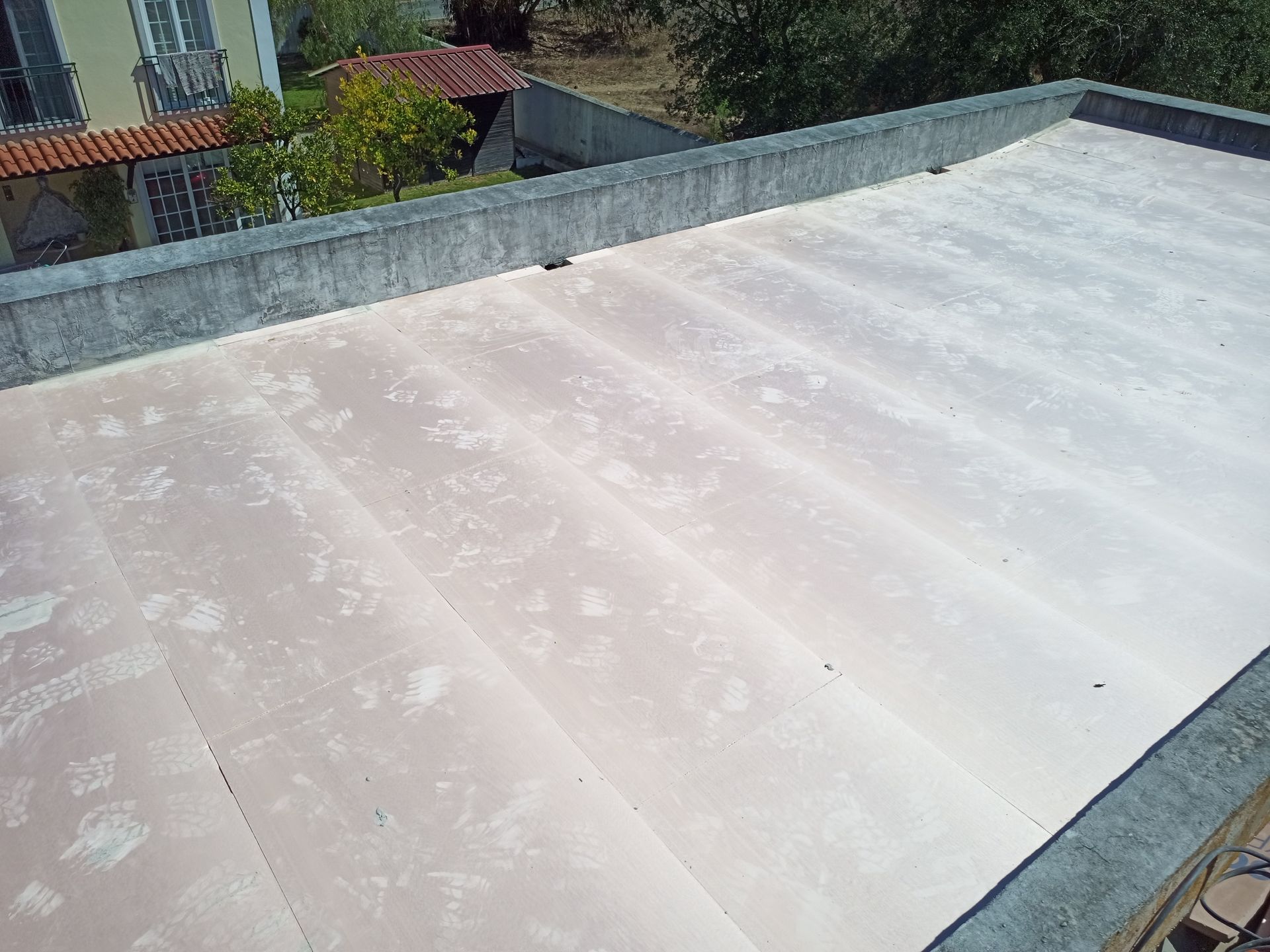 Cobertura plana com painéis desbotados em tons de branco e rosa, cercada por uma borda de concreto, e edifícios visíveis ao fundo.