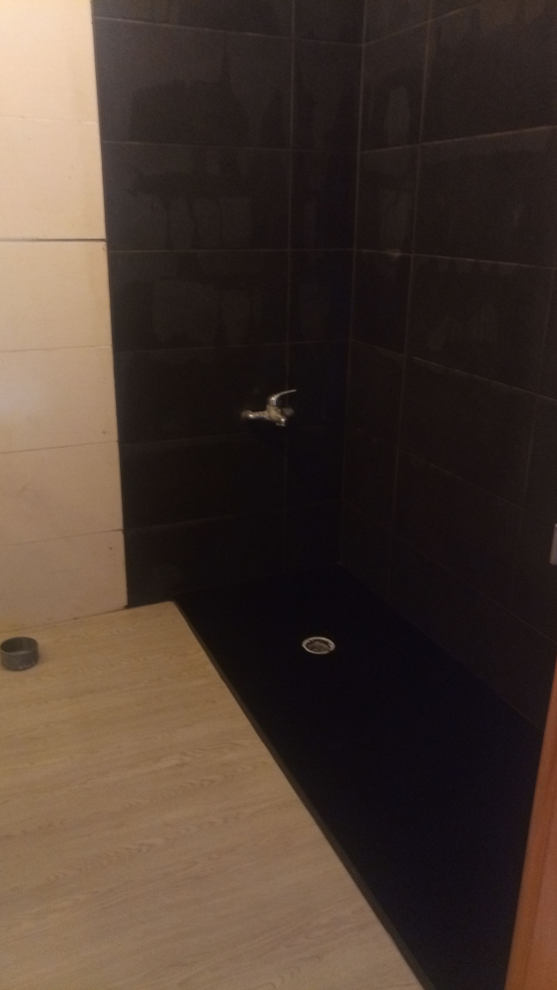 Box de chuveiro com azulejos pretos e torneira prateada. Bancada bege em primeiro plano.