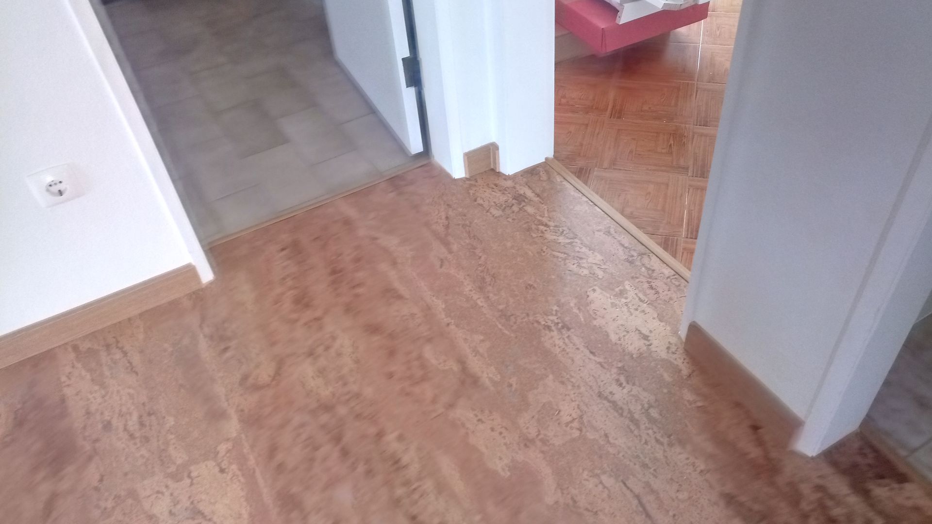 Corredor com piso de madeira, moldura da porta e paredes brancas.