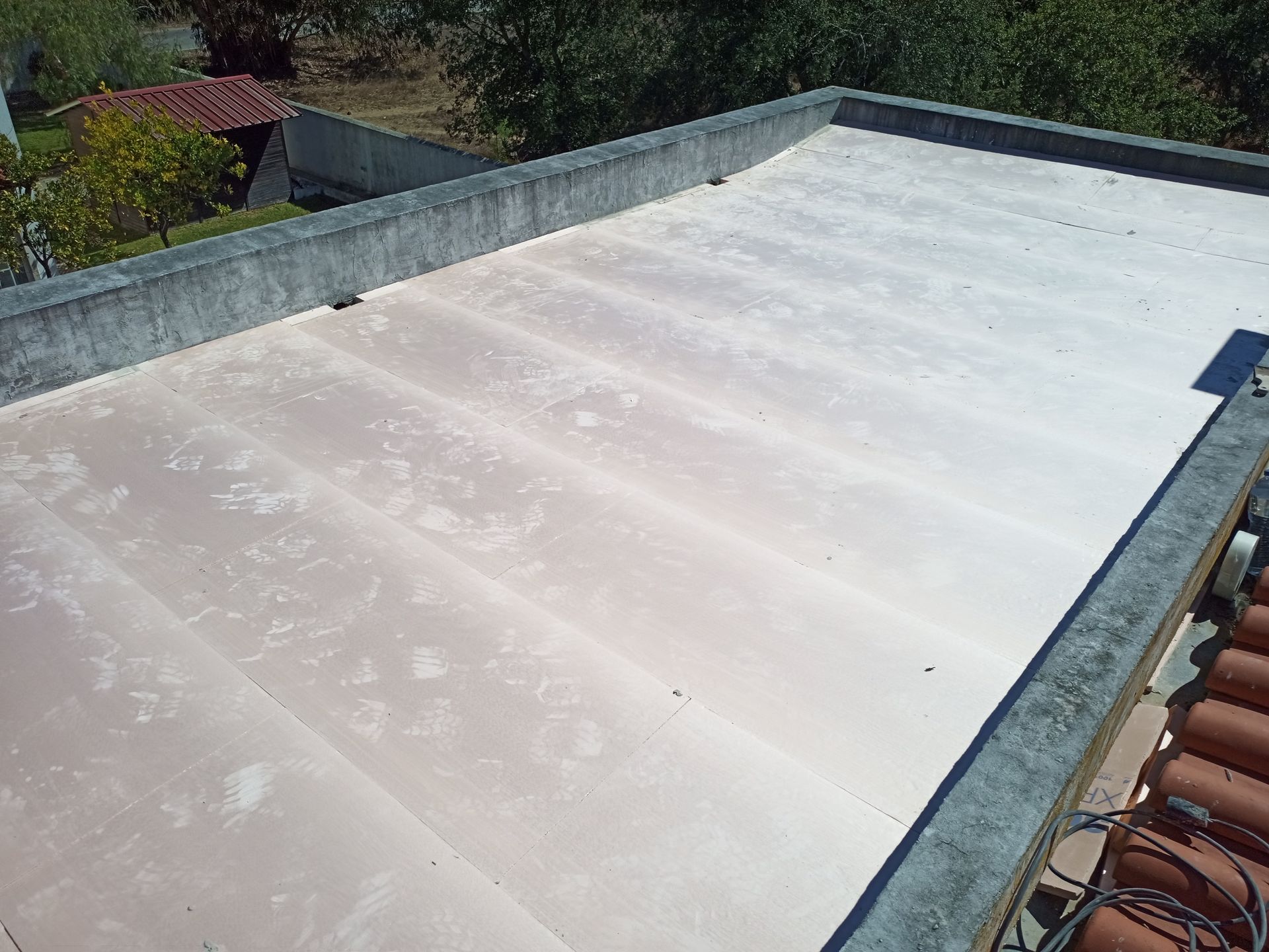 Telhado plano e claro com borda de concreto; algumas árvores são visíveis ao fundo.