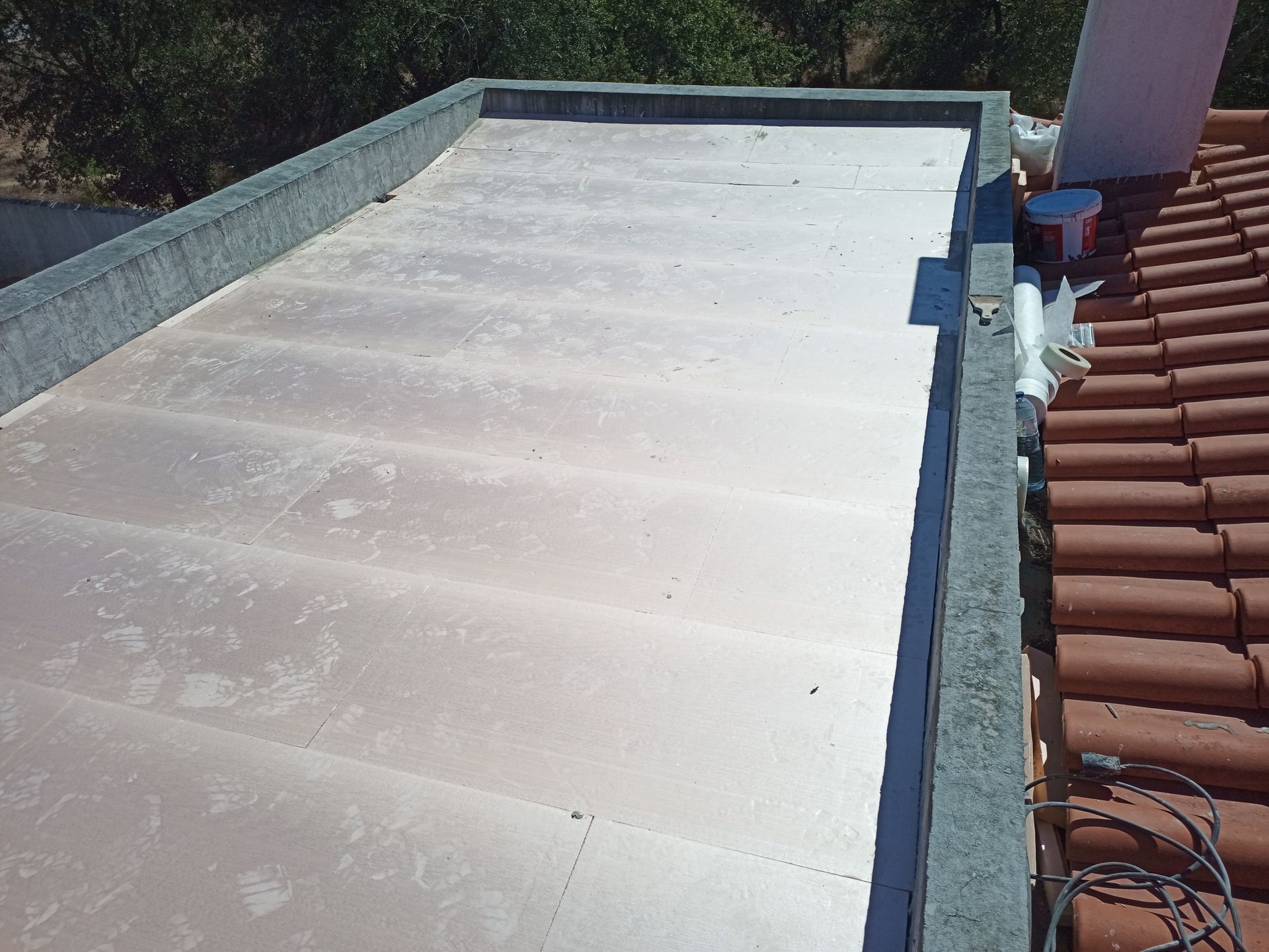 Painéis isolantes rosa instalados em um telhado plano, ao lado de um telhado de telhas.