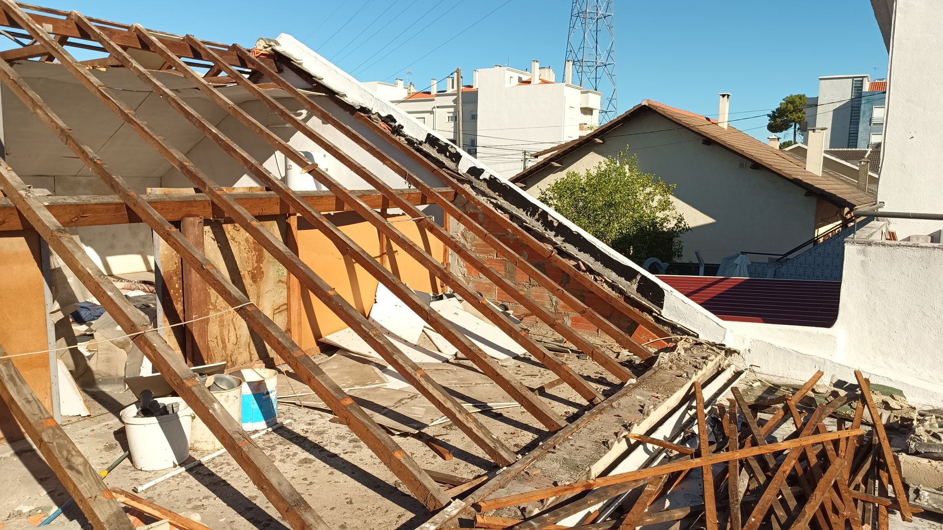 Telhado parcialmente removido, mostrando vigas de madeira e destroços, com edifícios ao fundo.