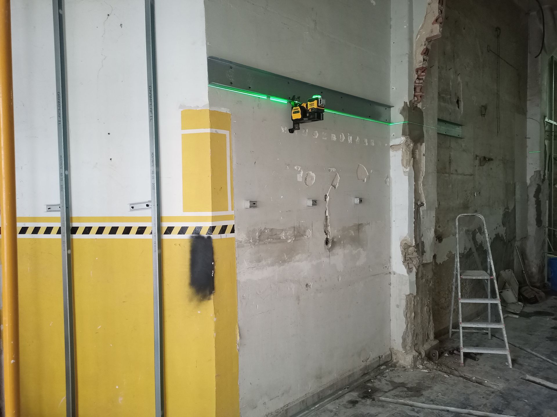 Durante a construção, um nível a laser projeta uma linha verde na parede. O interior apresenta paredes amarelas e brancas.