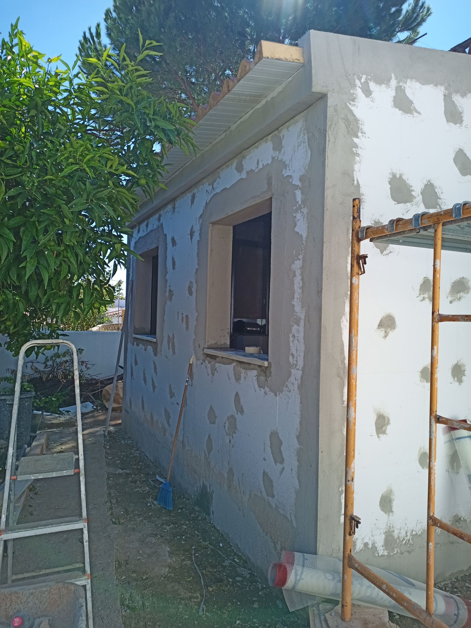 Fachada do prédio em construção, com duas janelas, andaimes e remendos de argamassa.