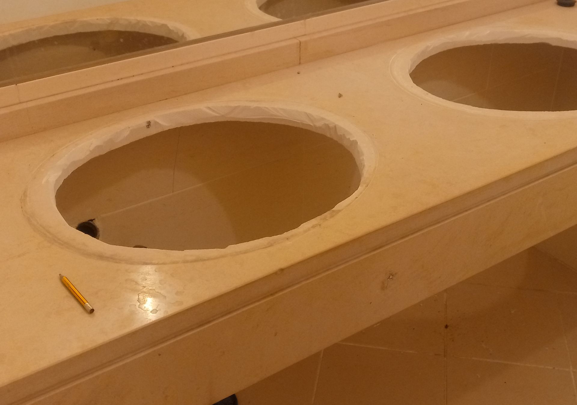 Bancada de banheiro com dois recortes para pia, em pedra clara sem acabamento.