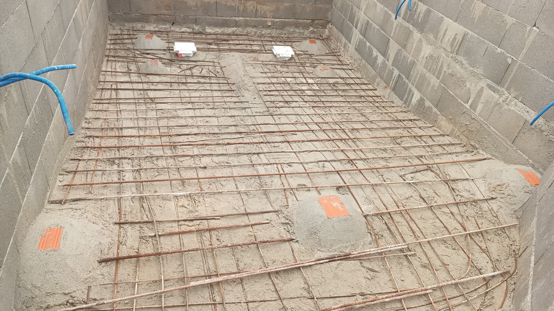 Interior de uma piscina de concreto em construção, com estrutura de vergalhões e encanamento.