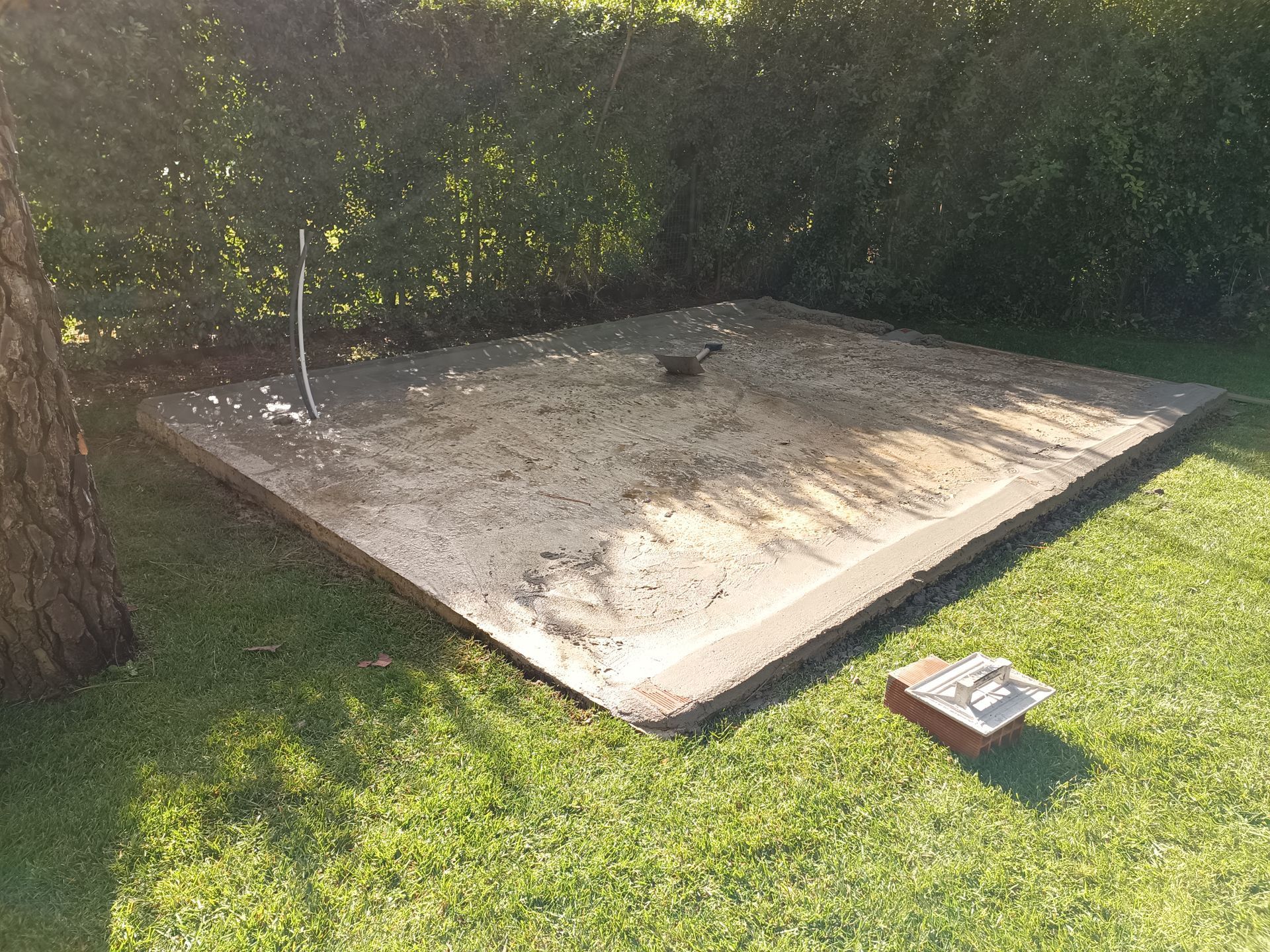 Placa de concreto em um gramado com um cano de metal e uma pequena estrutura de tijolos.