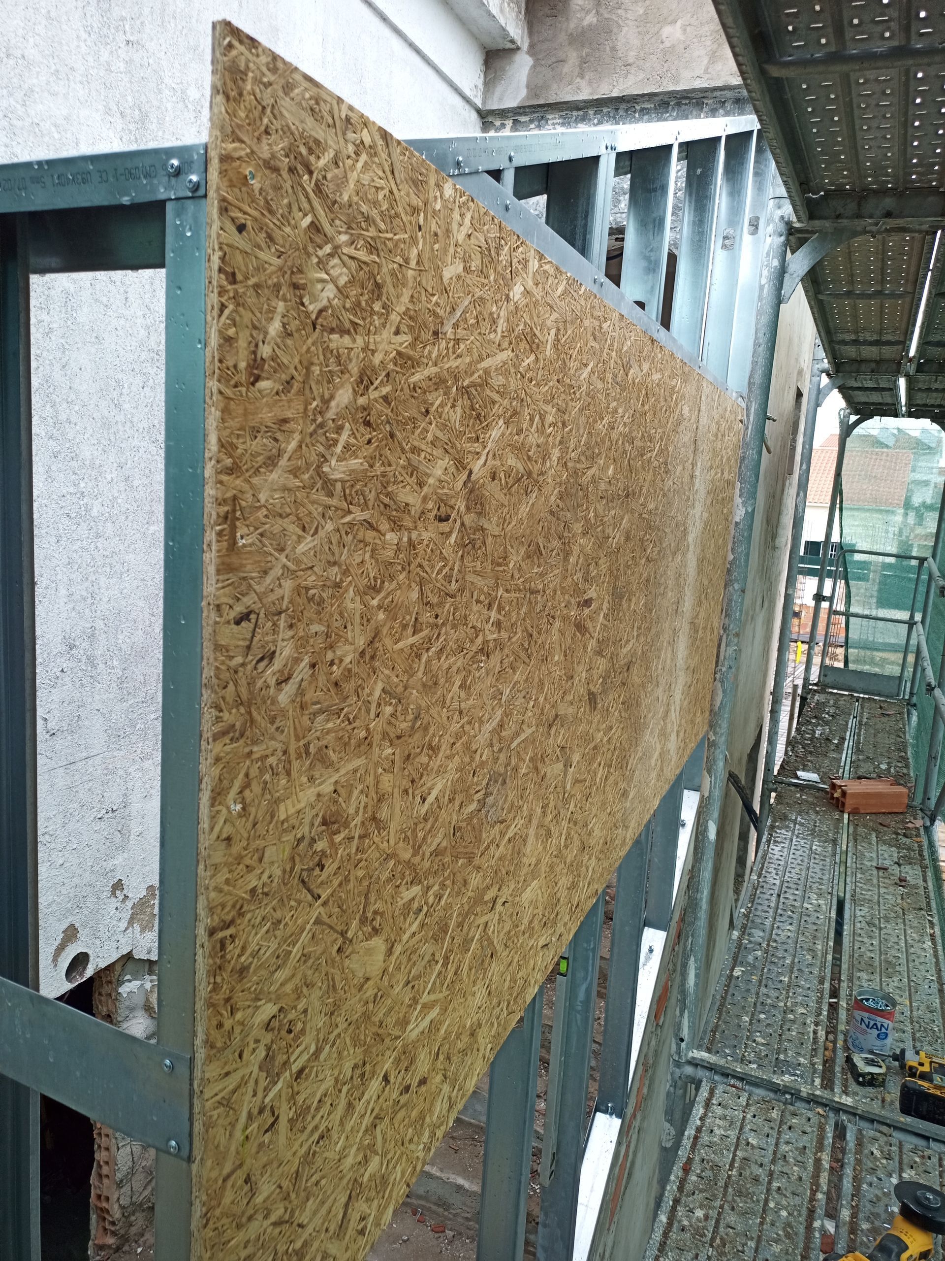 Grande painel de madeira fixado a uma estrutura metálica na fachada de um edifício durante a construção.