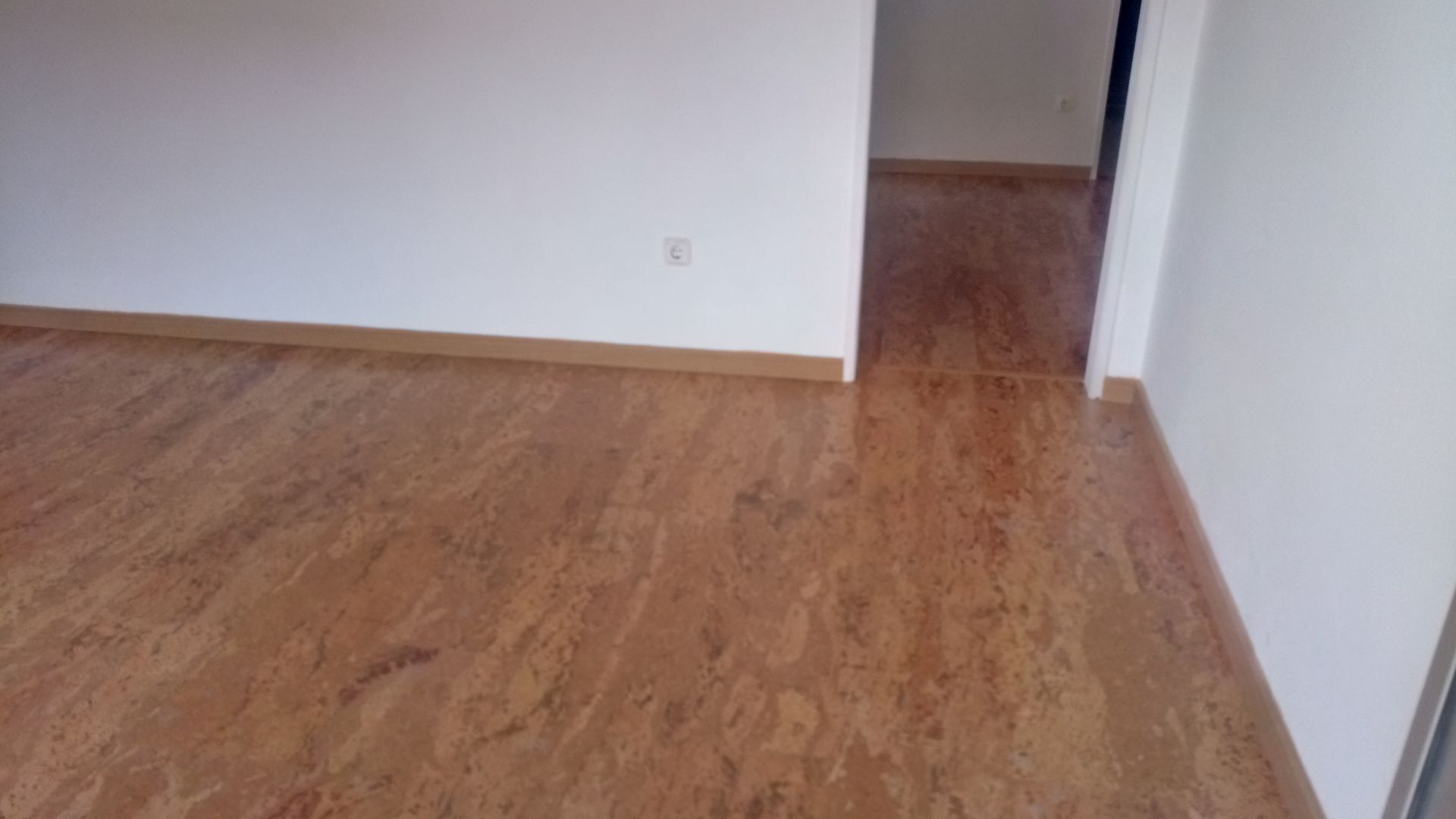 Piso de madeira maciça em um cômodo com paredes brancas e uma porta.