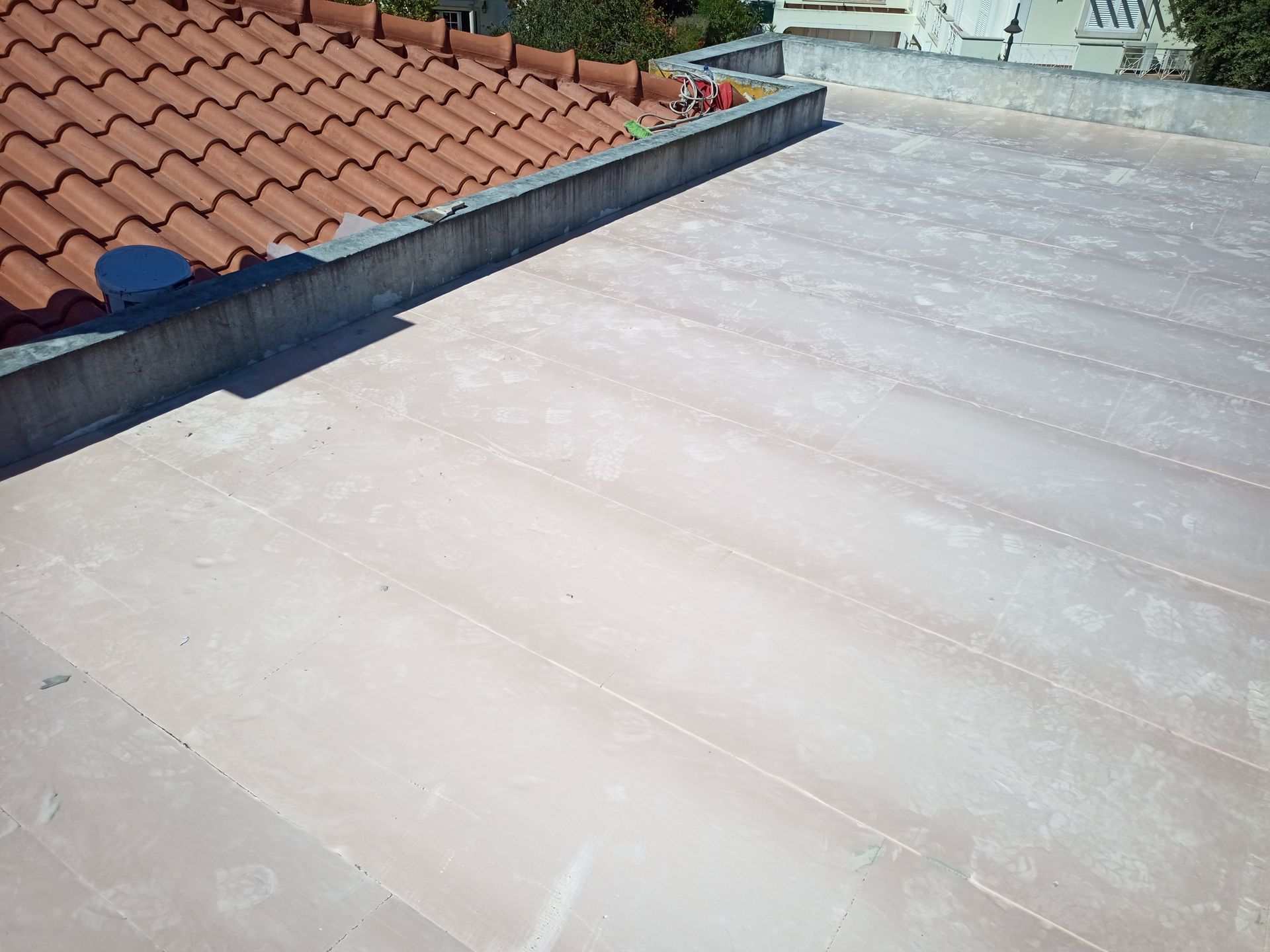 Borda de telhado de telha de terracota ao lado de um telhado plano com revestimento impermeável listrado em rosa claro.