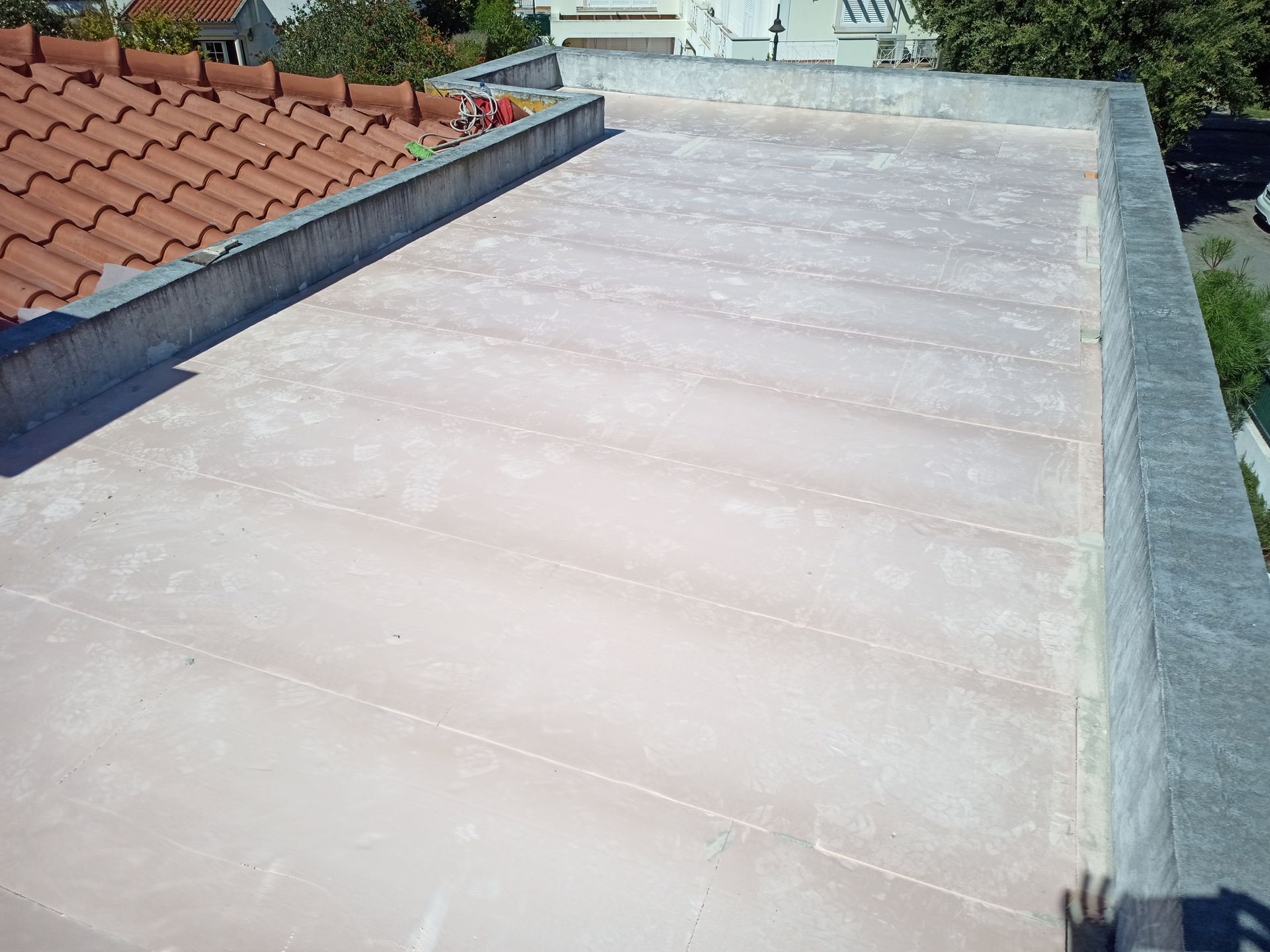 Telhado plano com revestimento rosa claro, bordas de concreto e telha vermelha visível à esquerda.