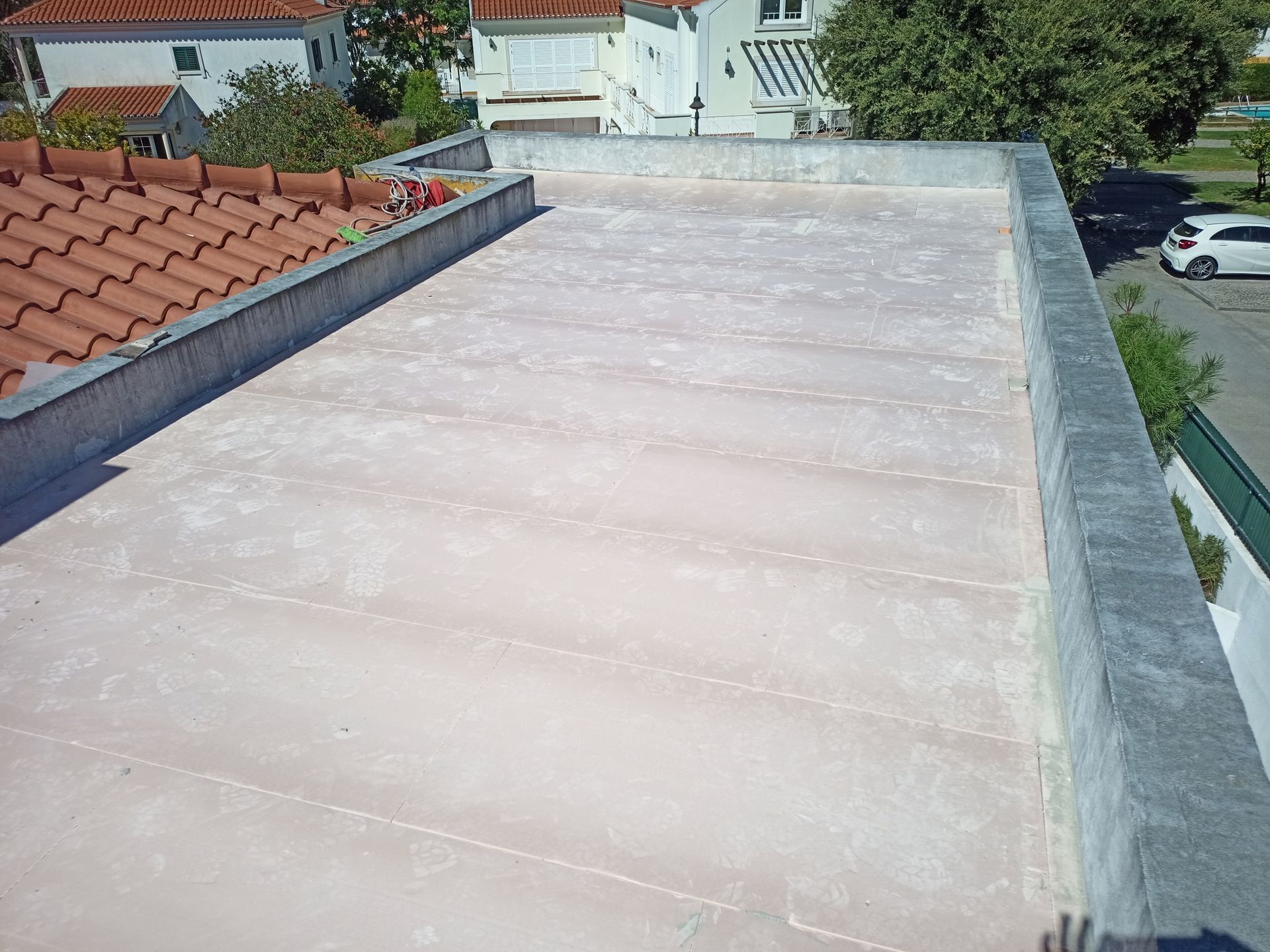 Cobertura plana com superfície rosa claro, bordas de concreto e vista parcial para casas e rua.