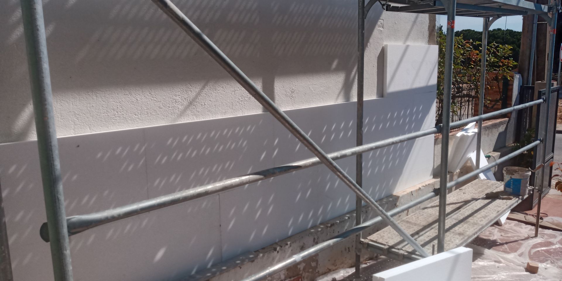 Andaimes junto a uma parede branca com sombras, possivelmente durante uma construção ou renovação.