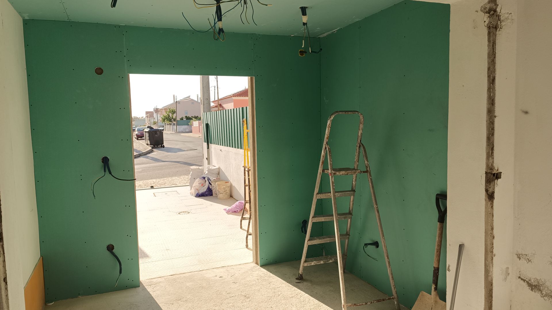 Quarto interno em construção, com drywall verde ao redor da porta. Escada dentro.