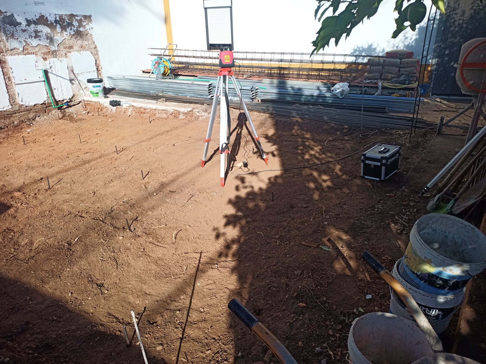 Canteiro de obras com equipamento de topografia instalado em terra marrom, ferramentas visíveis.