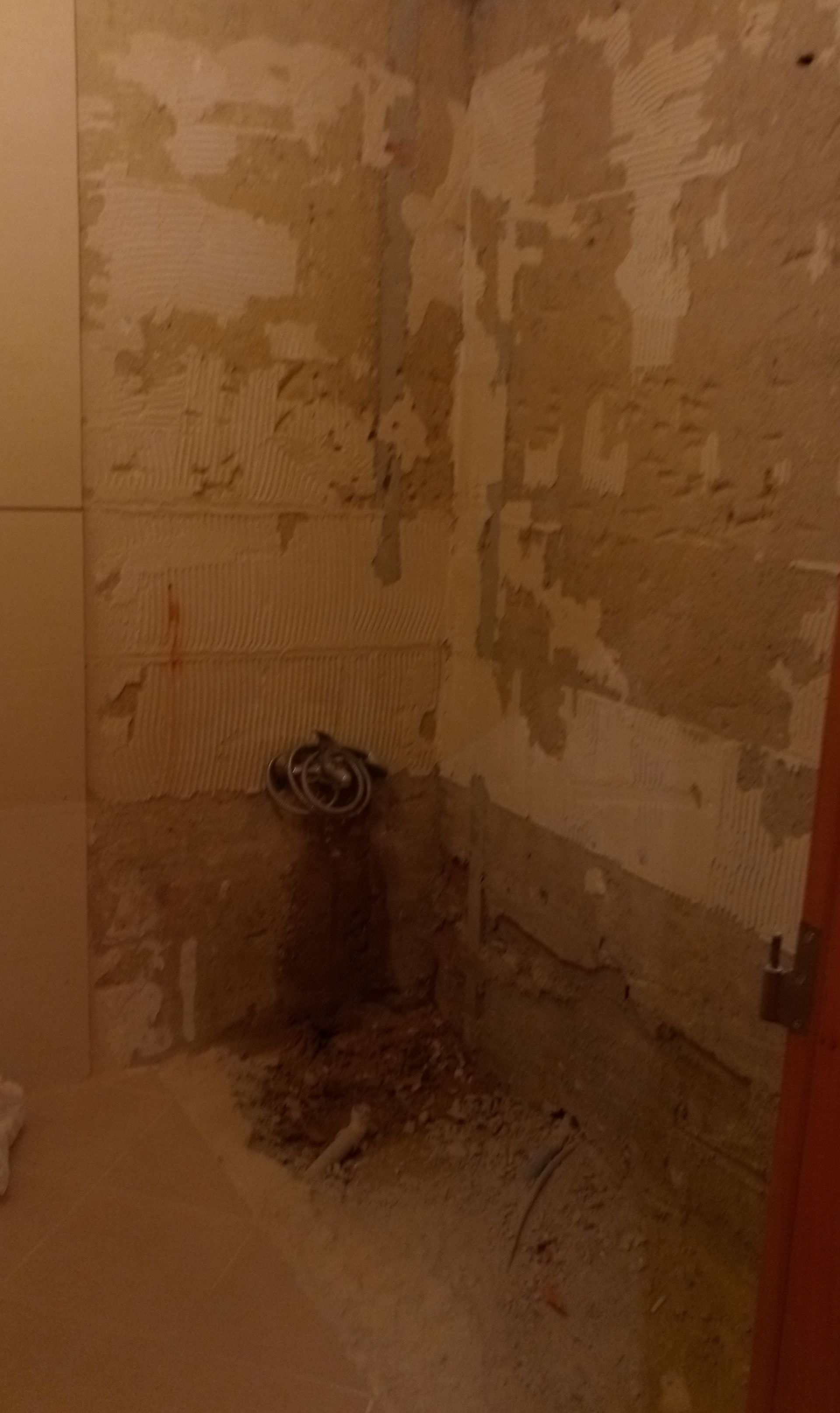 Parede do banheiro com azulejos removidos, mostrando o encanamento e o gesso danificado.