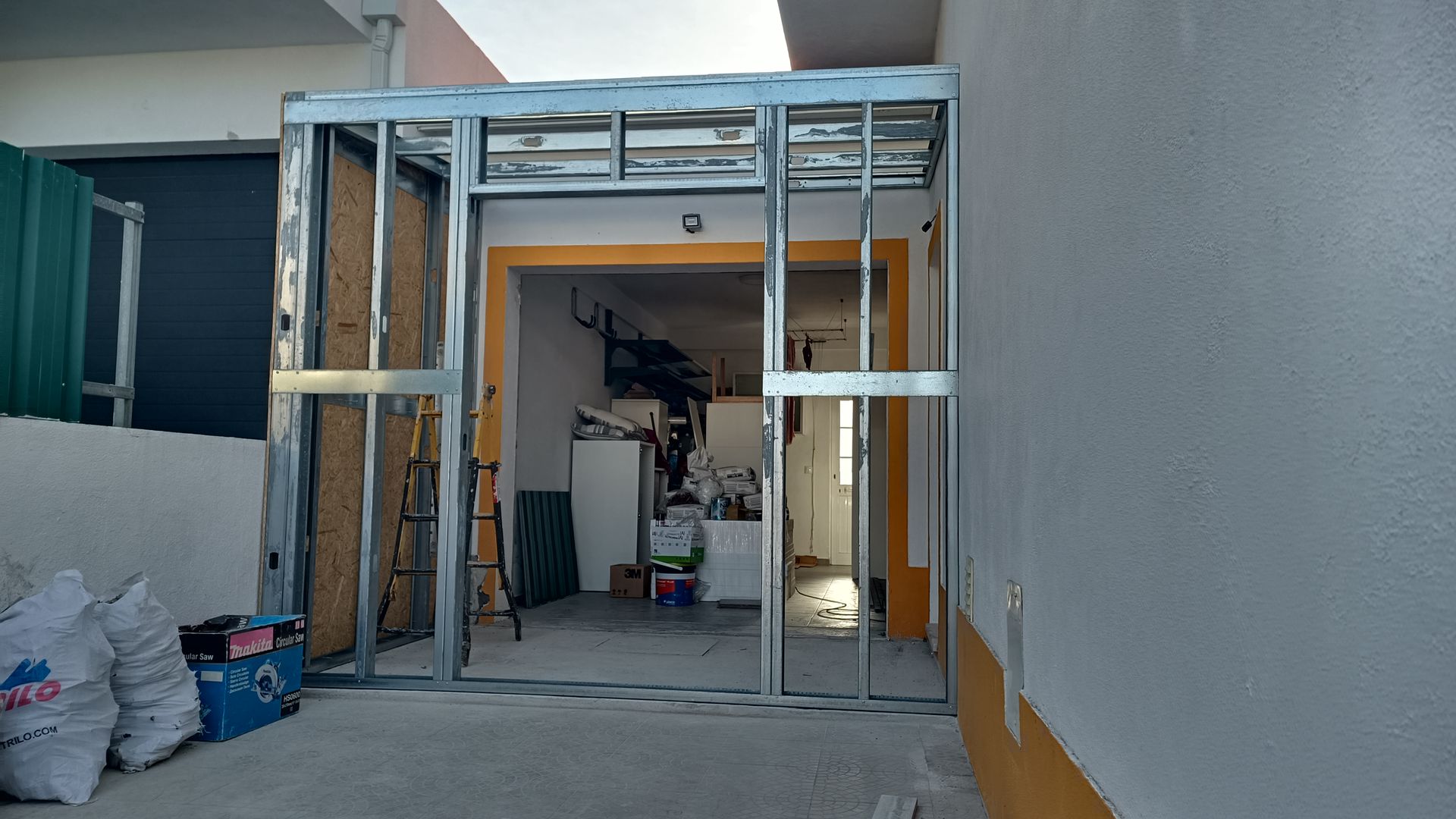 Estrutura metálica para porta e paredes laterais, área externa com vista para um cômodo.