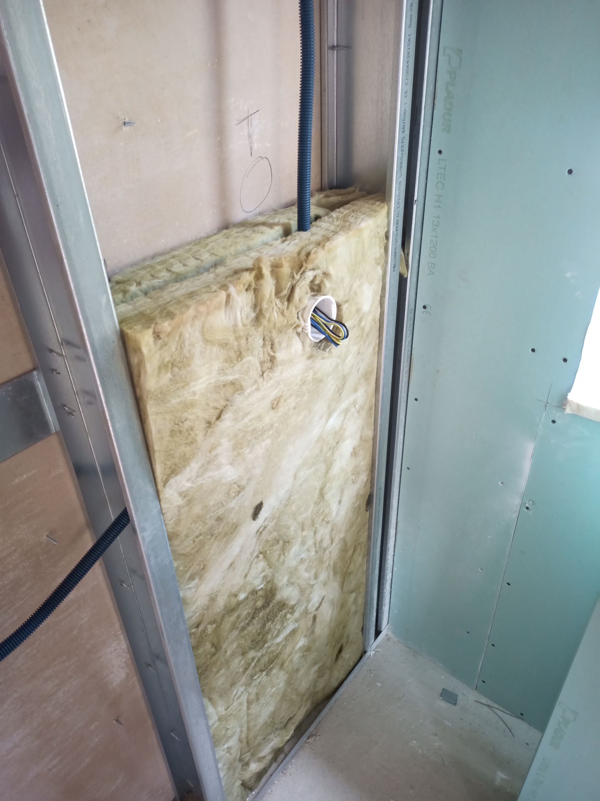 Construção de parede interna com isolamento entre perfis metálicos e fiação elétrica.