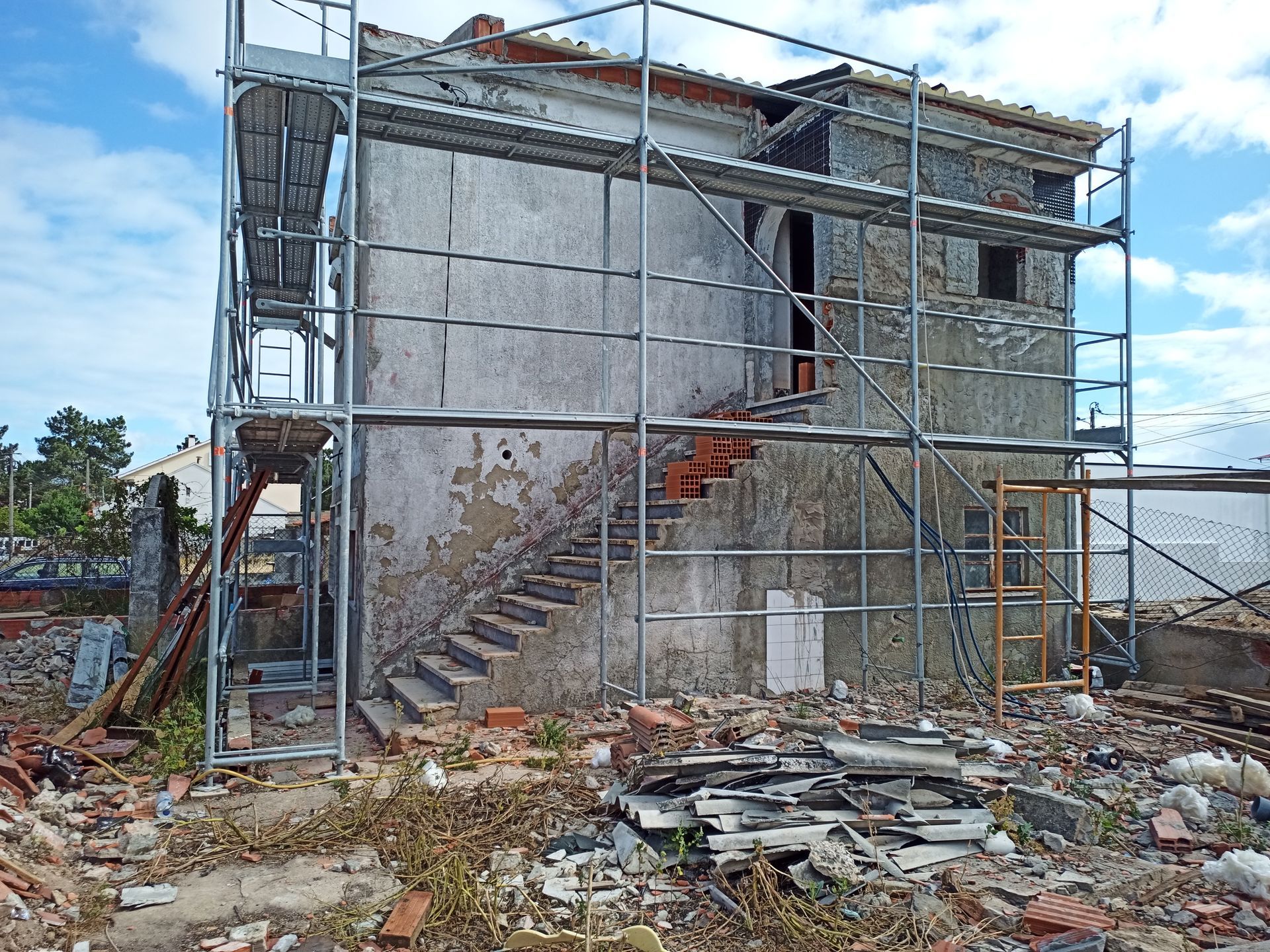 Fachada de prédio com andaimes durante reforma, entulho no chão, céu nublado.