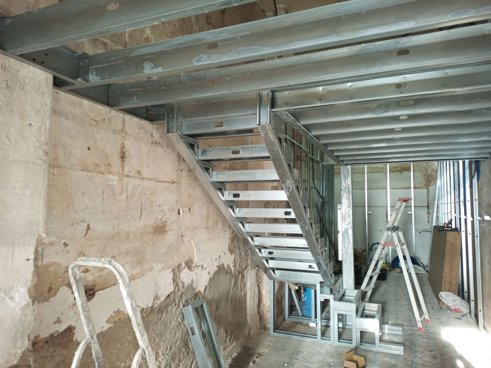 Escada com estrutura metálica em construção, com estrutura e vigas de suporte visíveis. Cenário da obra.