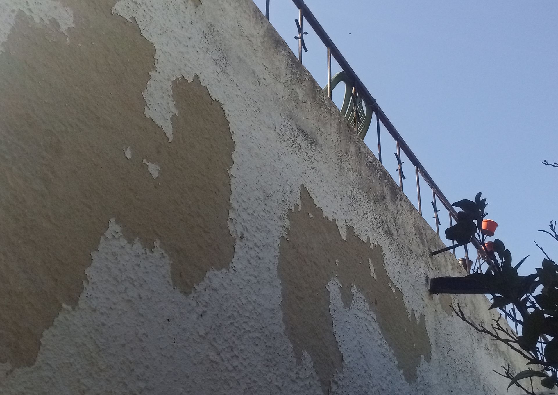 Parede externa com tinta descascando; grade de metal acima, céu azul claro.