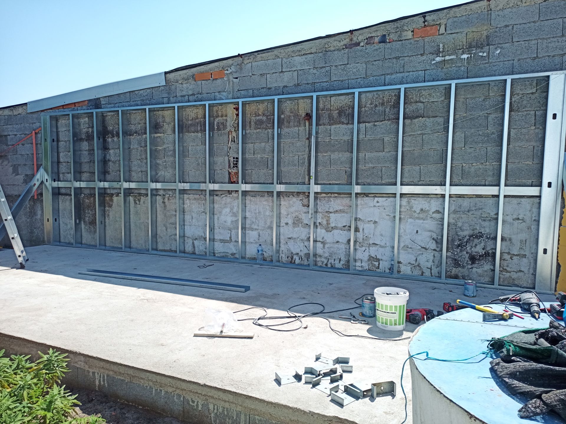 Estrutura metálica de parede contra uma parede de tijolos desgastados sobre uma superfície de concreto.