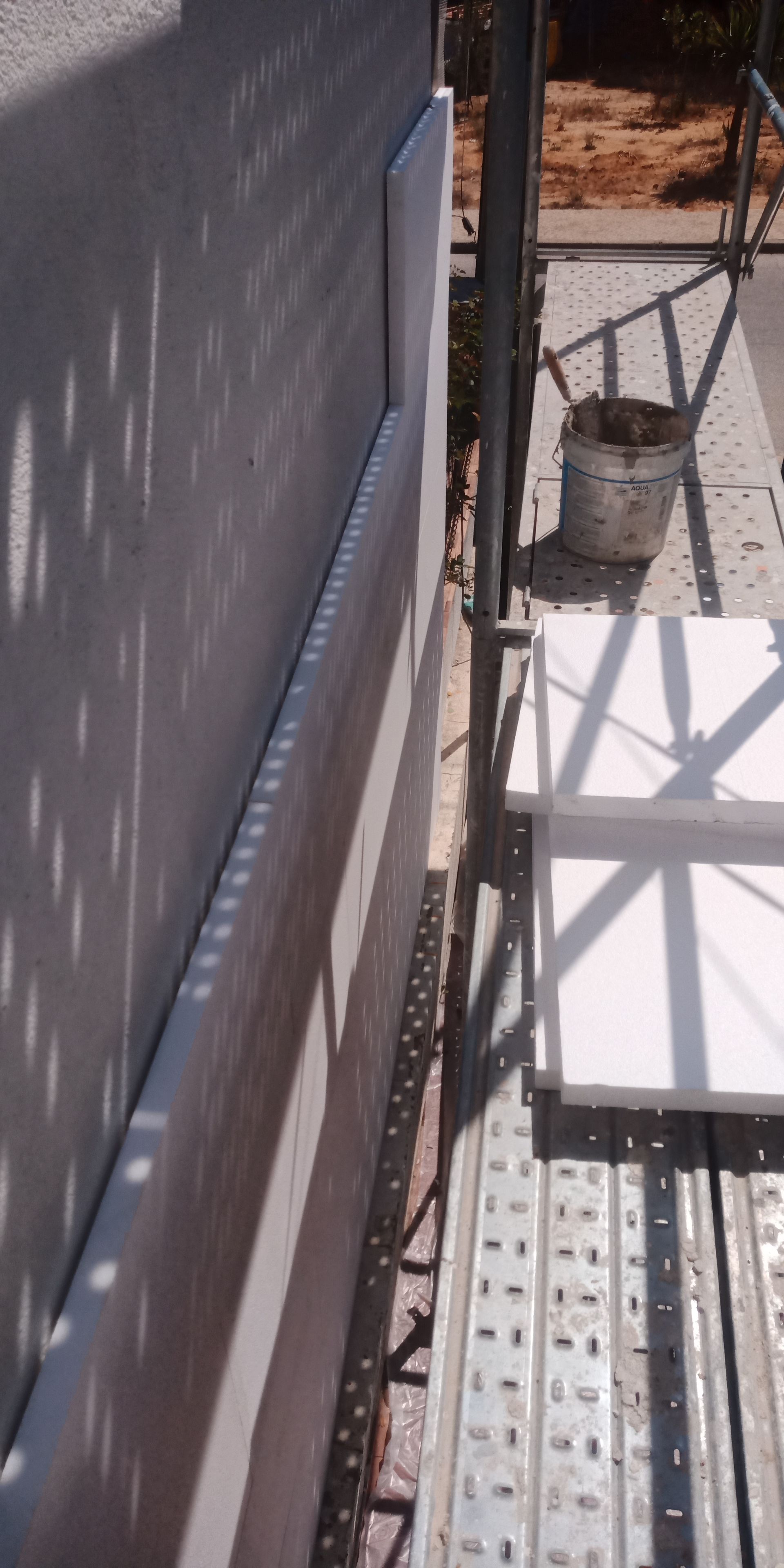 Canteiro de obras com andaimes e isolamento de paredes. A luz do sol projeta sombras.