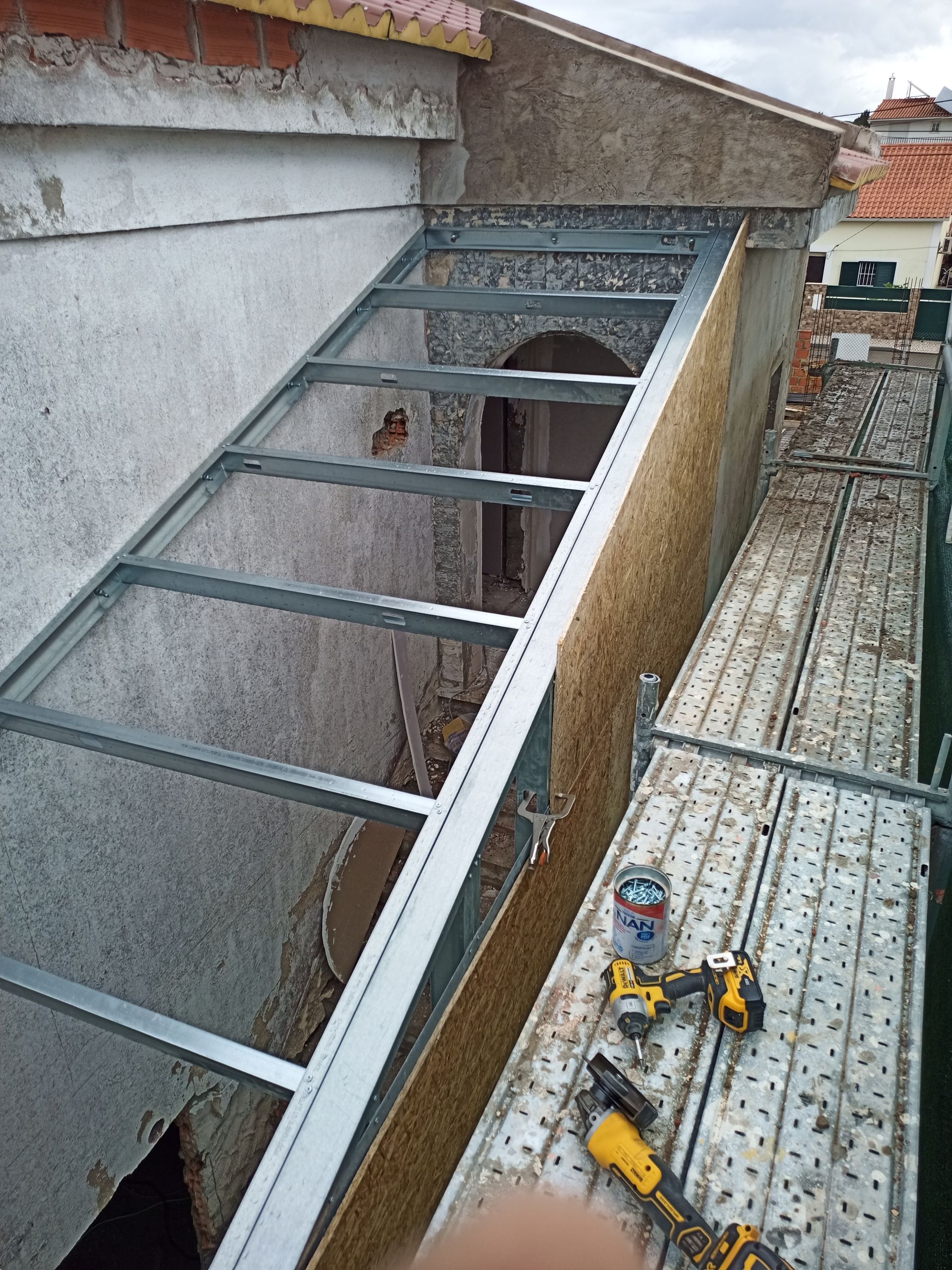 Cobertura com estrutura metálica em construção na parte externa de um prédio, com ferramentas e andaimes próximos.