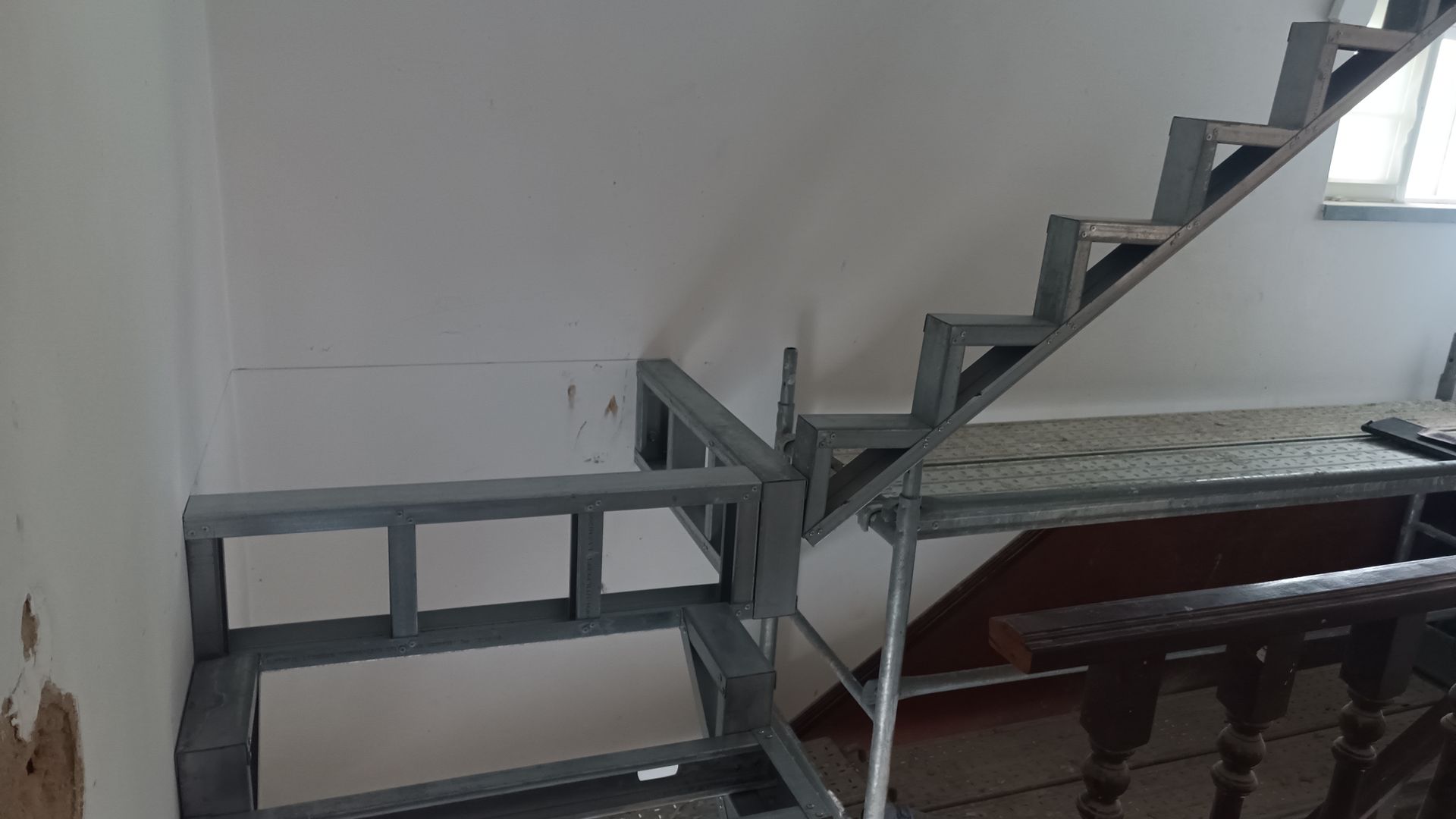 Estrutura metálica de escada contra uma parede branca; construção inacabada.