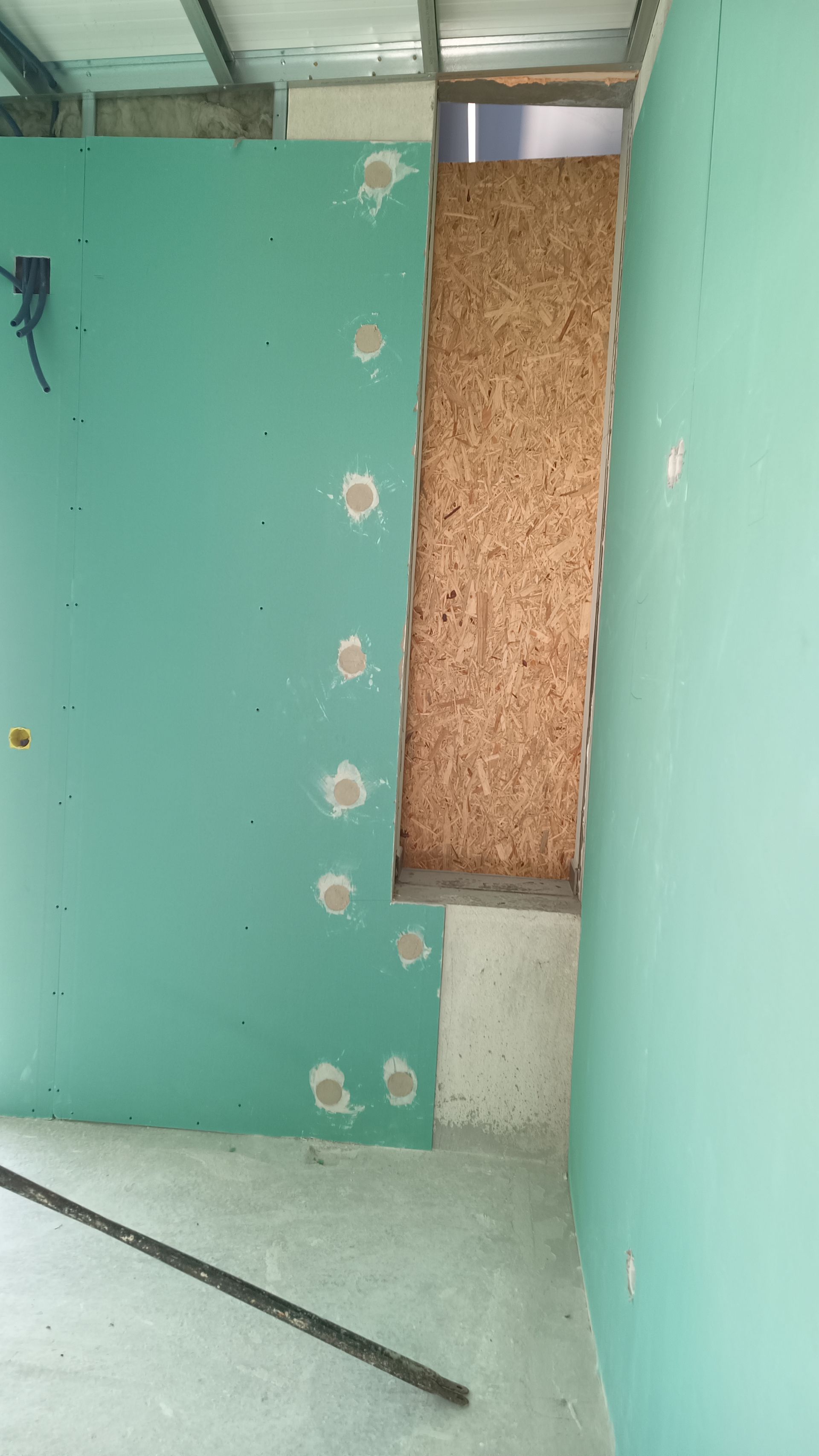 Construção interior: Paredes de gesso cartonado verde, painéis de madeira, porta aberta, cômodo inacabado.