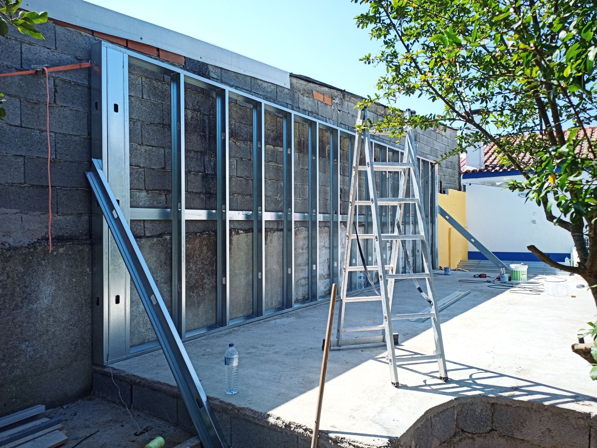 Estrutura metálica para parede fixada a uma estrutura de blocos de concreto; uma escada está próxima.